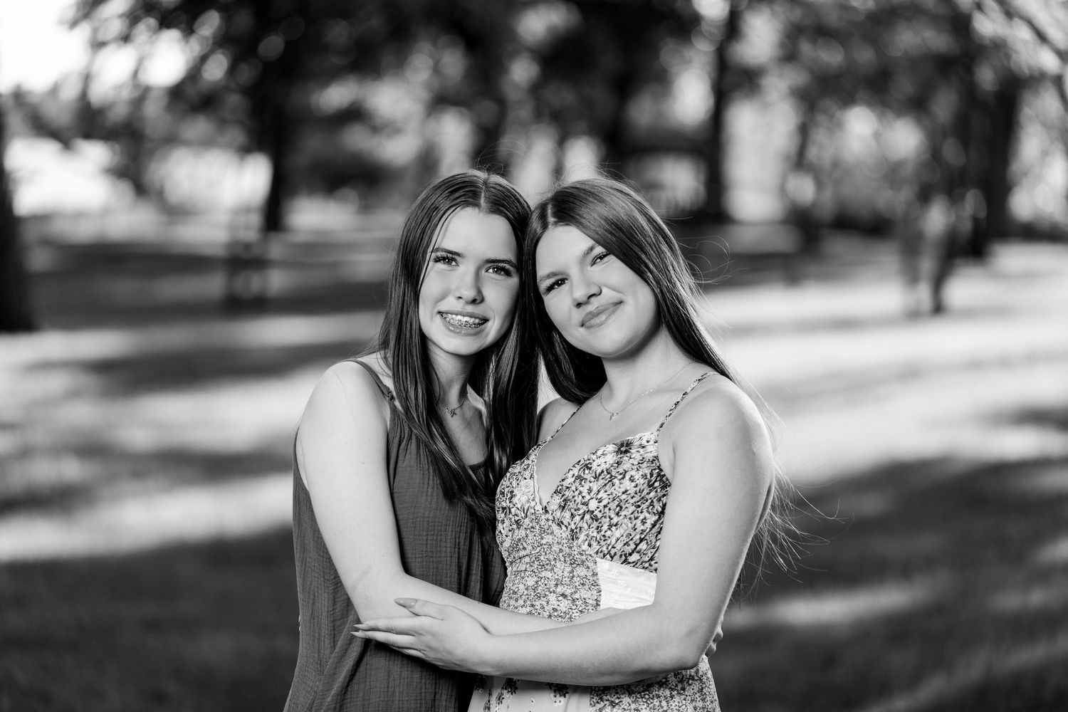 Black and white portrait of two teenage girls embracing and smiling outdoors in a park.