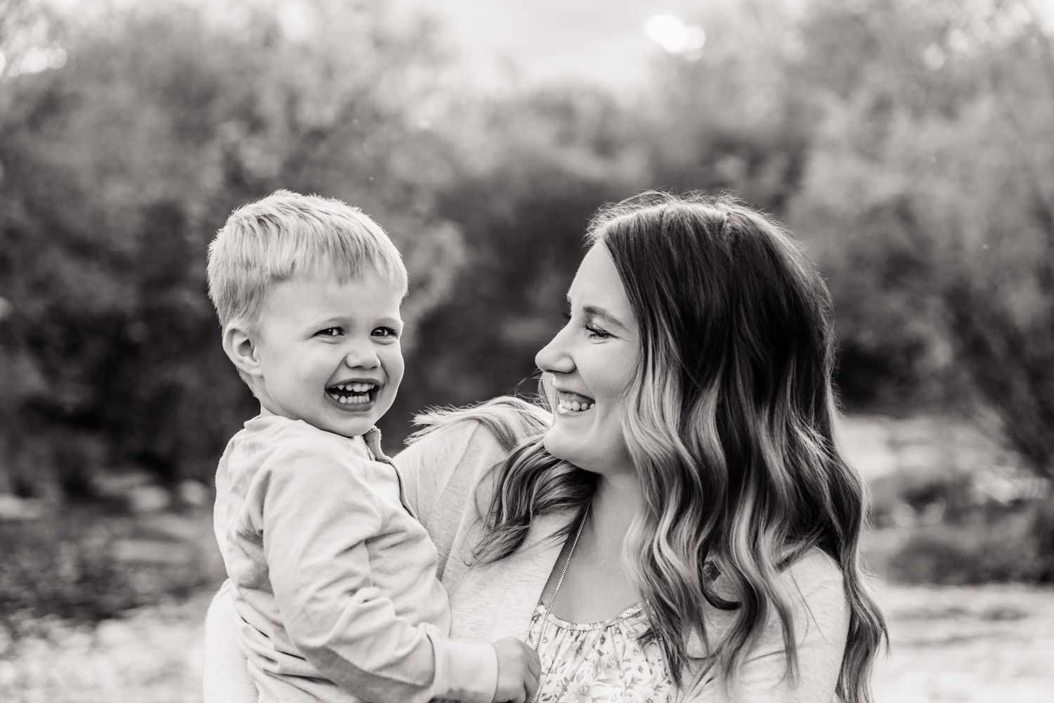 Black and white photo of a laughing toddler boy being held by a smiling young woman outdoors.