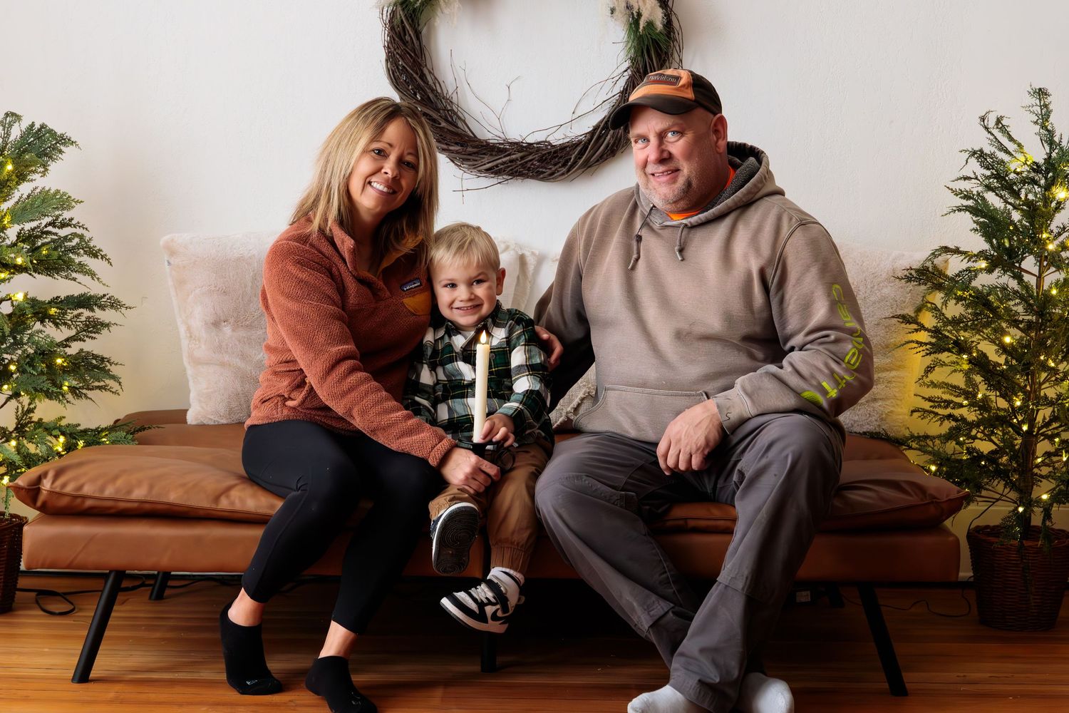 Family sitting together on bench with holiday wreath and decorations in background.