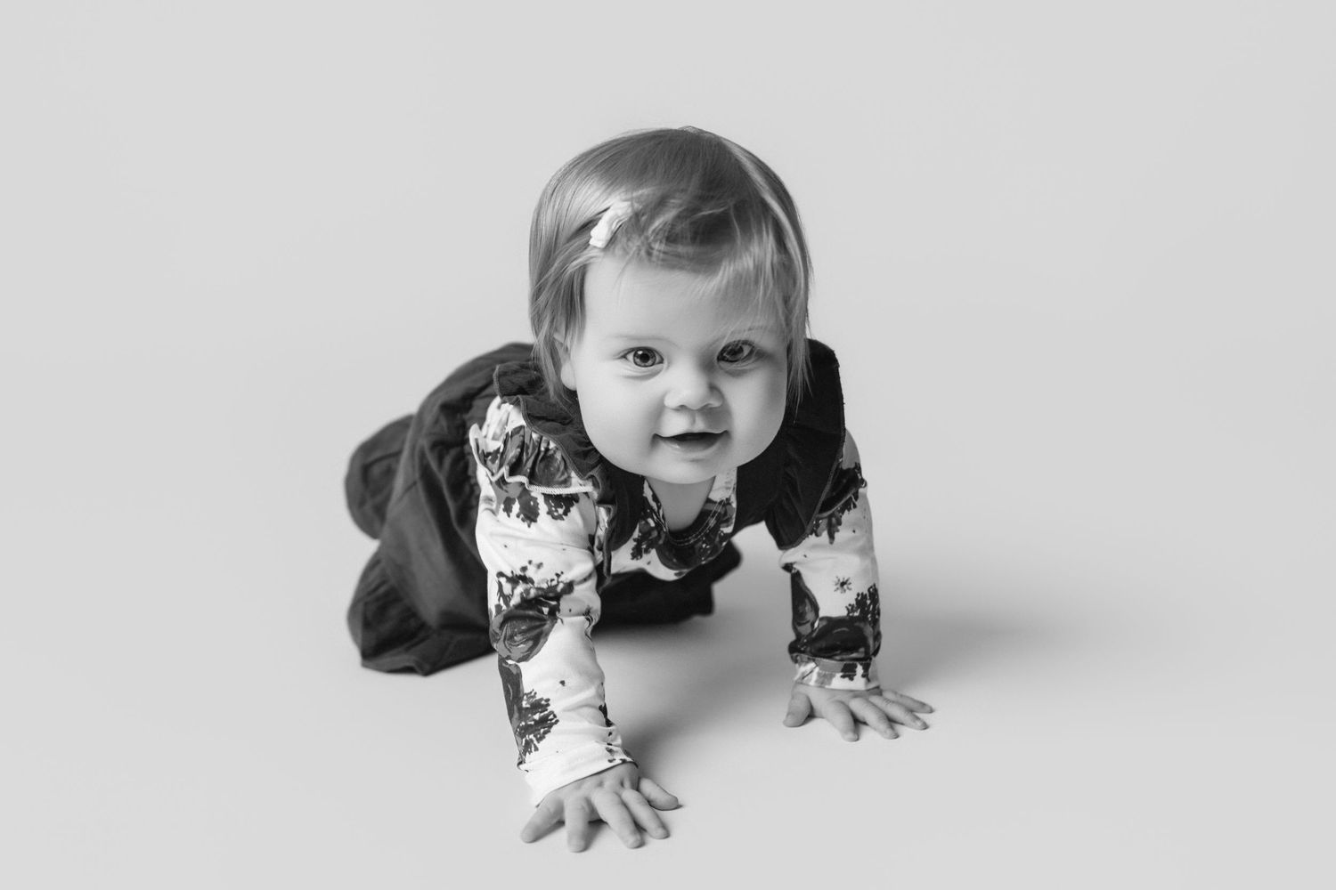 A baby in a patterned outfit crawls on a white background.