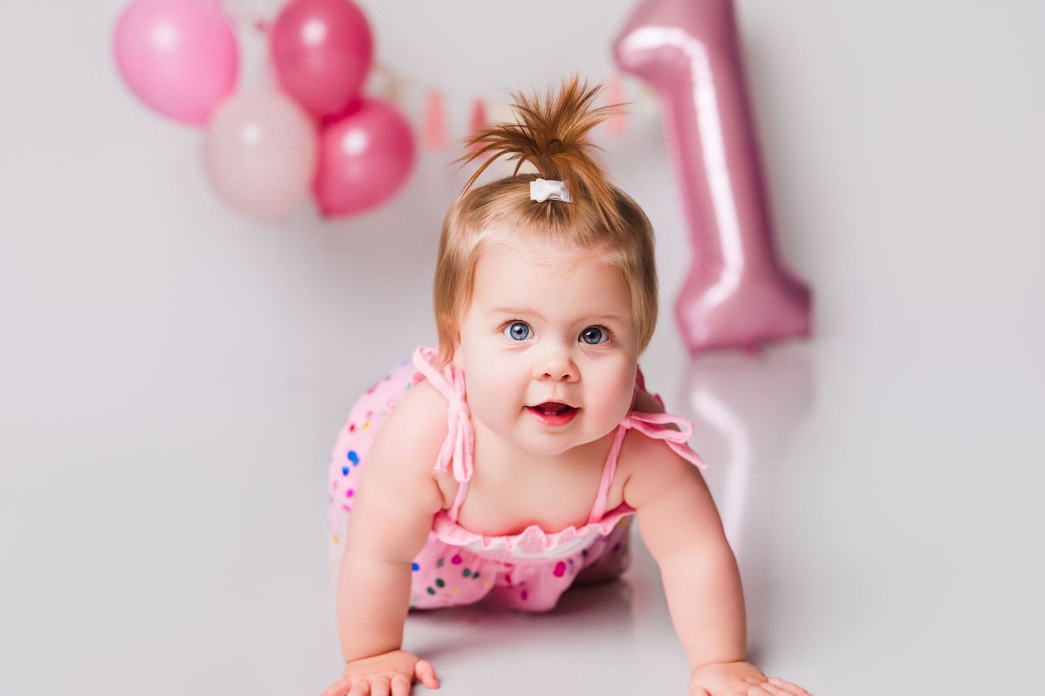 Happy baby celebrating first birthday with pink balloons and party decorations.
