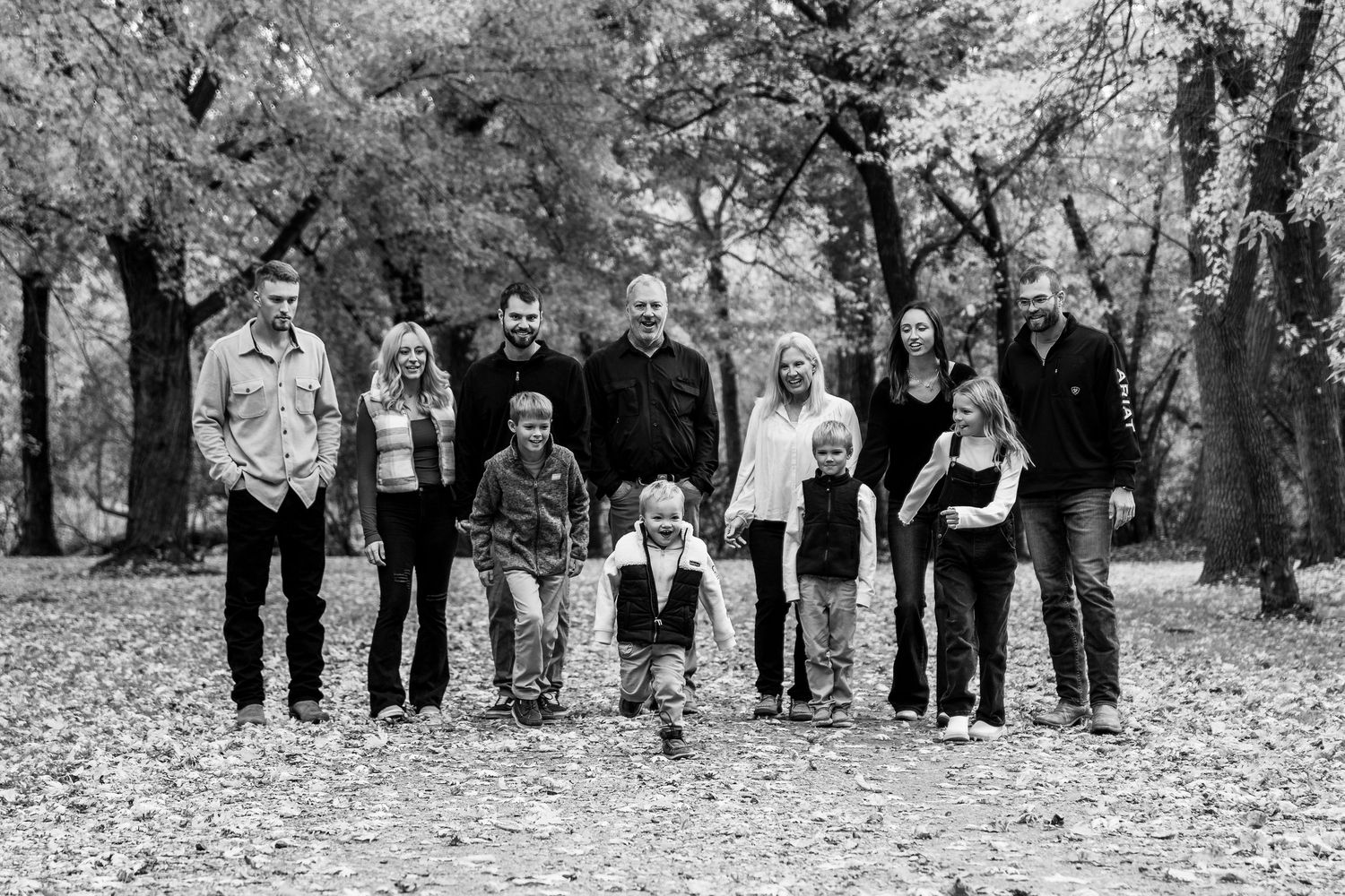 Large group poses together in line during autumn photoshoot with fallen leaves.