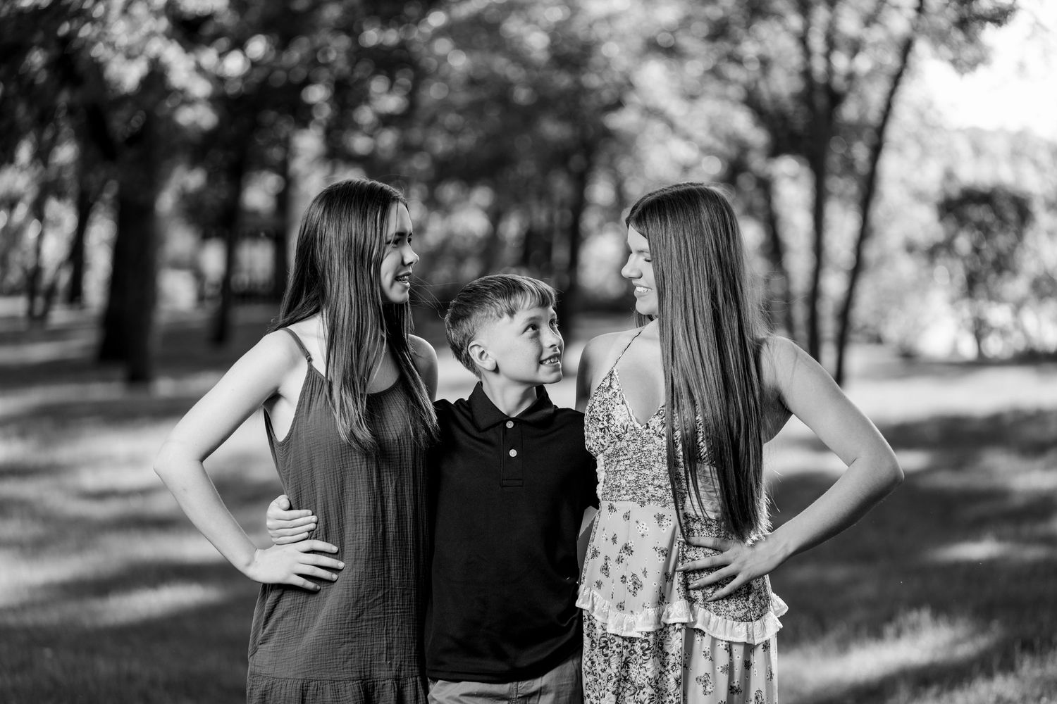 Black and white photo of a woman and three children laughing together in a sunny park setting.