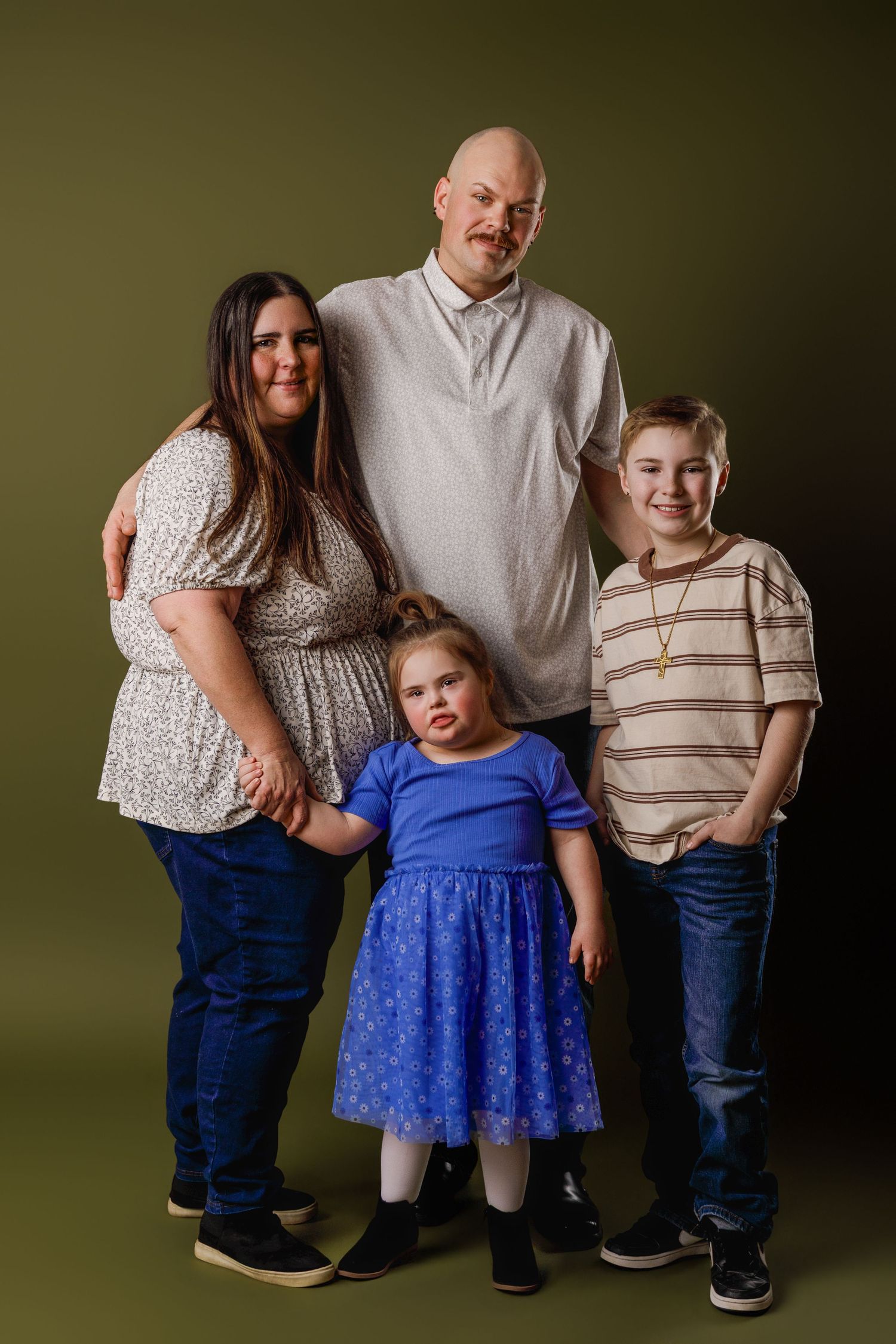 Family of four posing for a studio portrait against an olive green background, including two adults and two children.