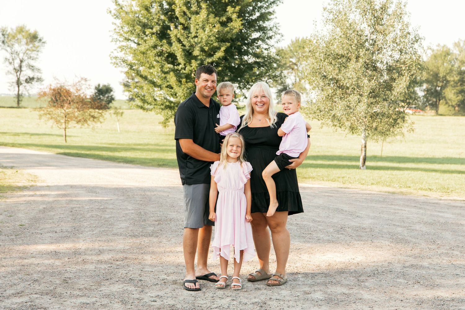 Small family group standing together outdoors on a sunny day with trees in the background.