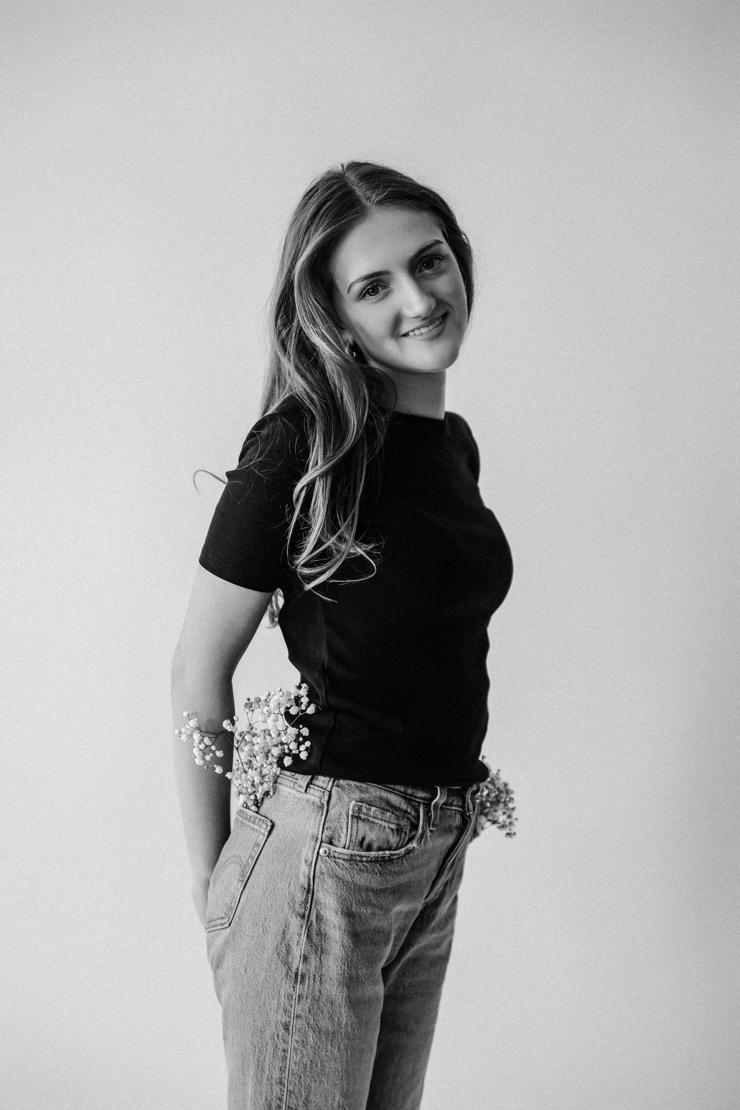 Black and white smiling woman in black tee and jeans with flowers in pockets, studio.