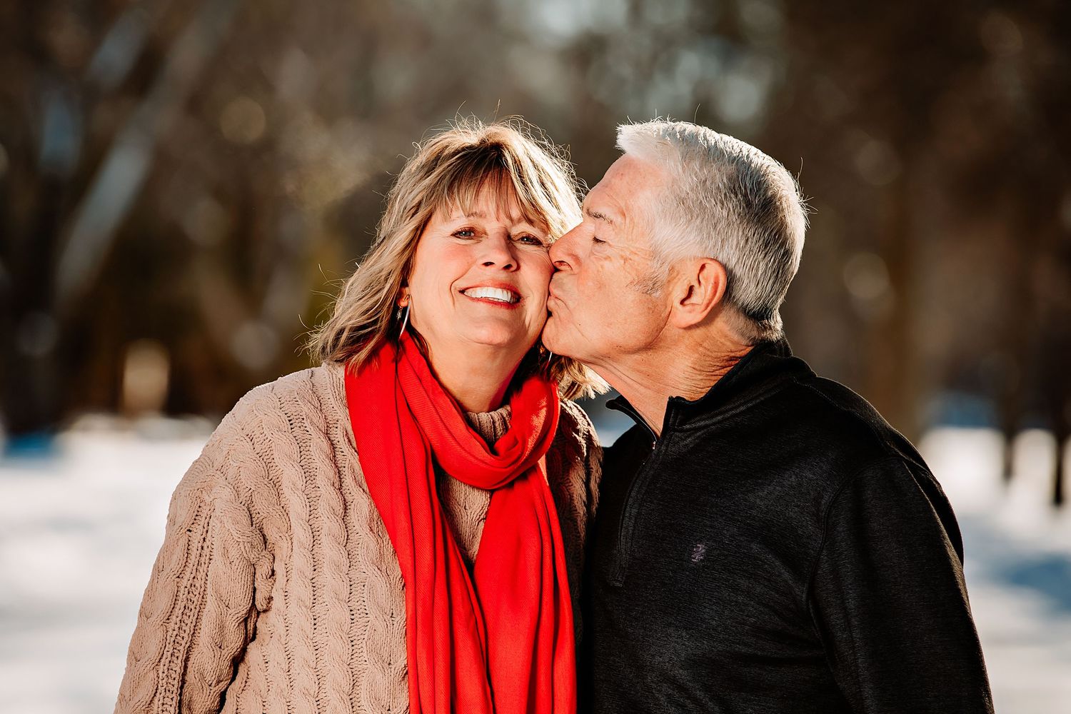 A couple shares an affectionate moment outdoors in winter with one wearing a bright red scarf.