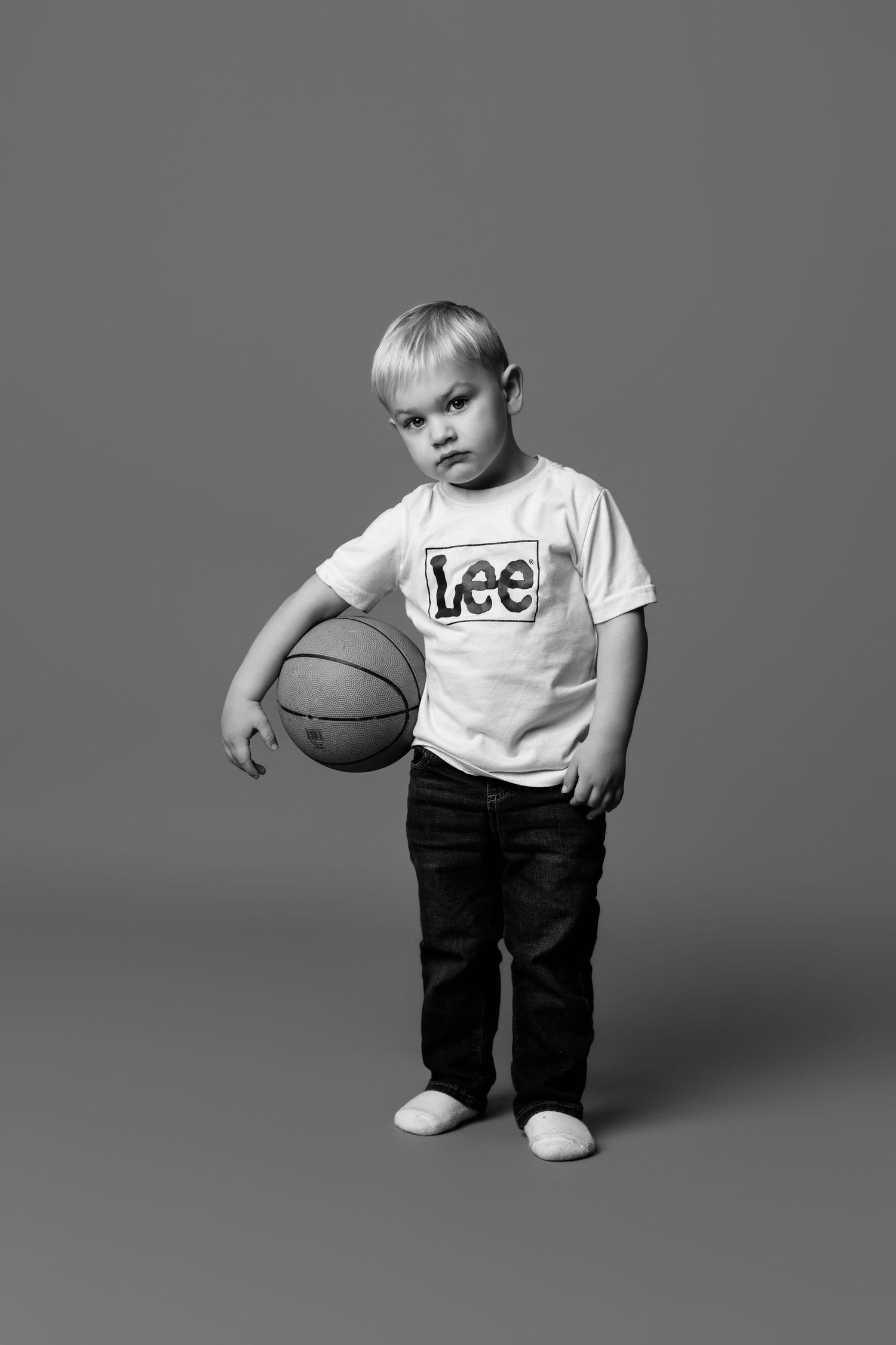 Black and white photo series of a young child in a Lee t-shirt playing with a basketball in different poses.
