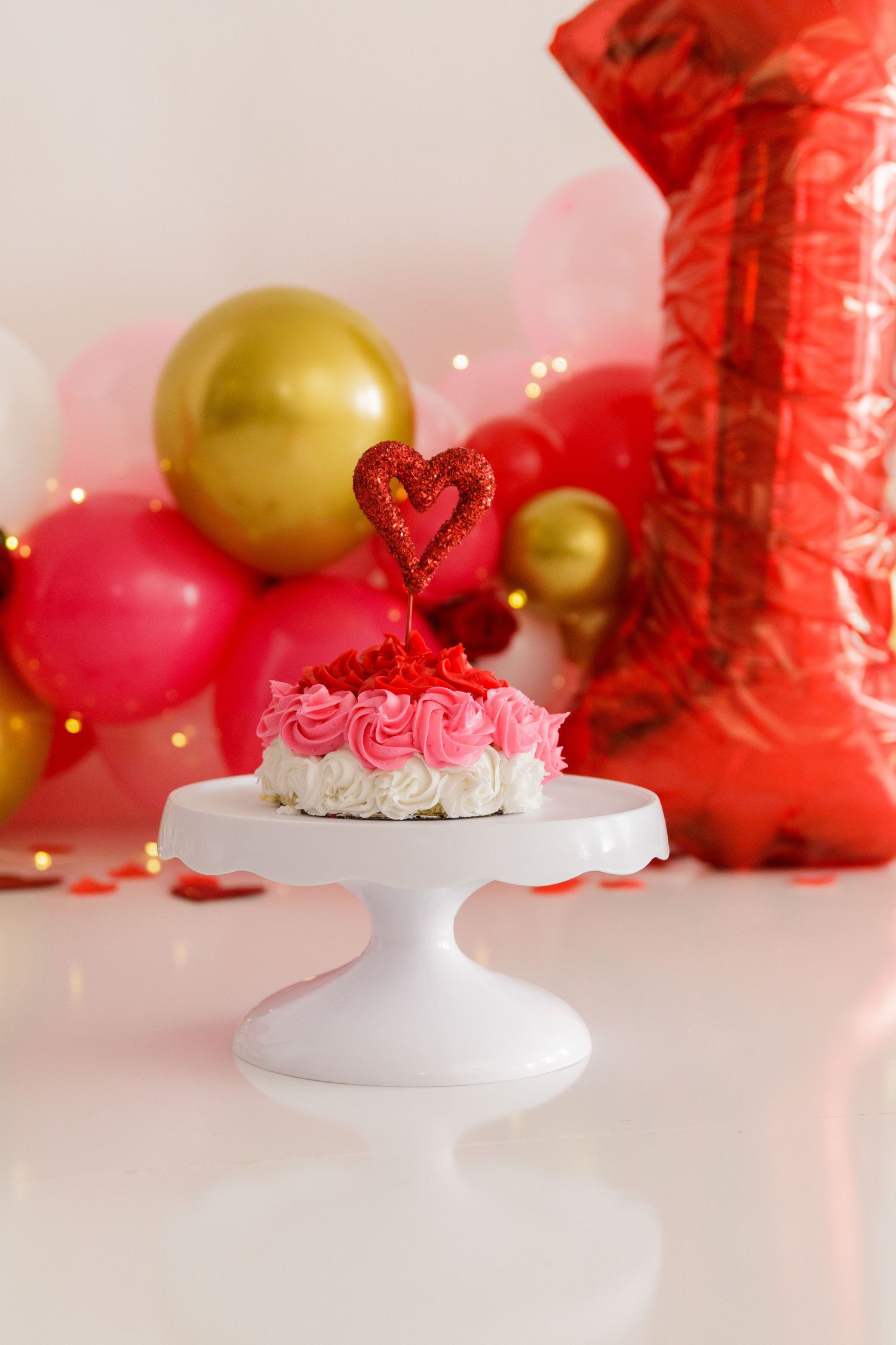 Valentine's Day themed dessert display with red and gold balloons and white cake stand.