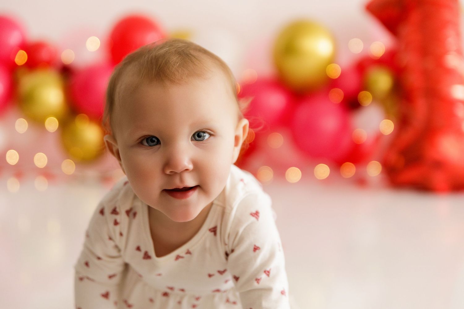 White and red heart-patterned outfit against Valentine's themed balloon backdrop.