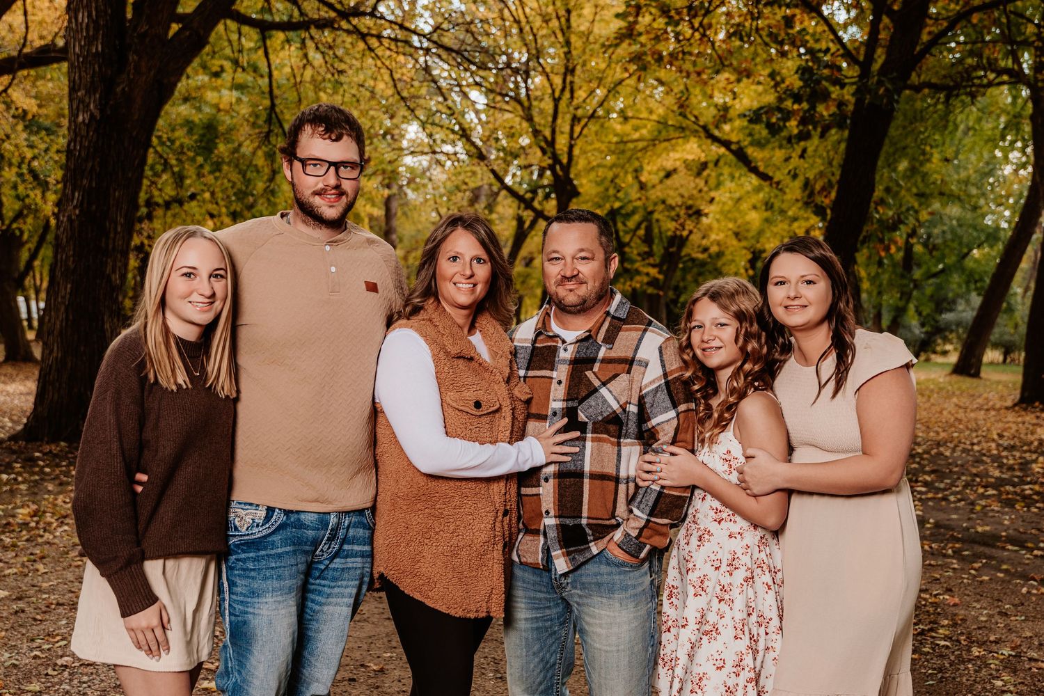 A group wearing coordinated brown and neutral tones poses together in an autumn outdoor setting.
