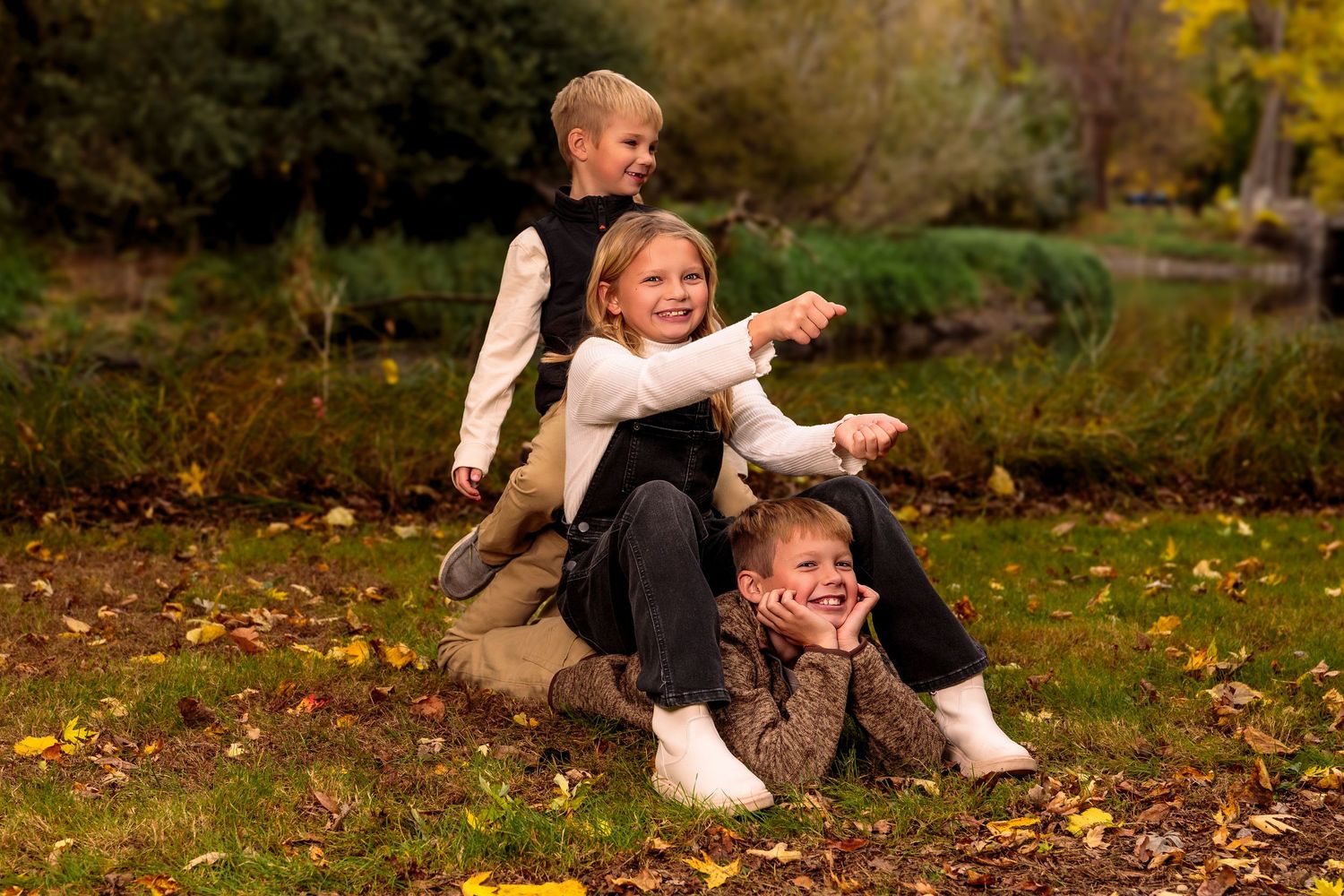 People enjoy a playful moment sitting among scattered fall leaves in a natural outdoor setting.