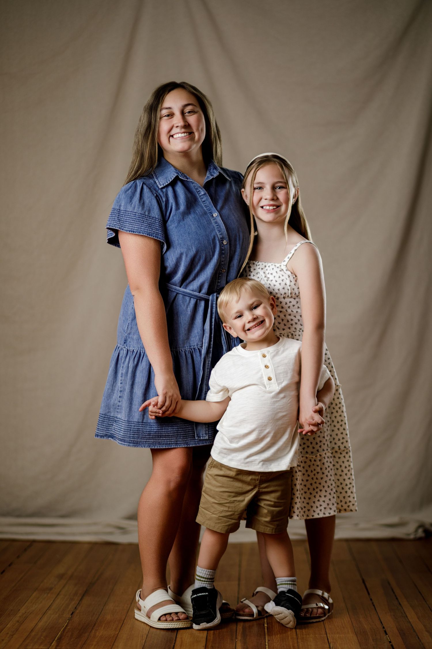Two girls and a young boy pose together smiling in a studio portrait on hardwood floors.