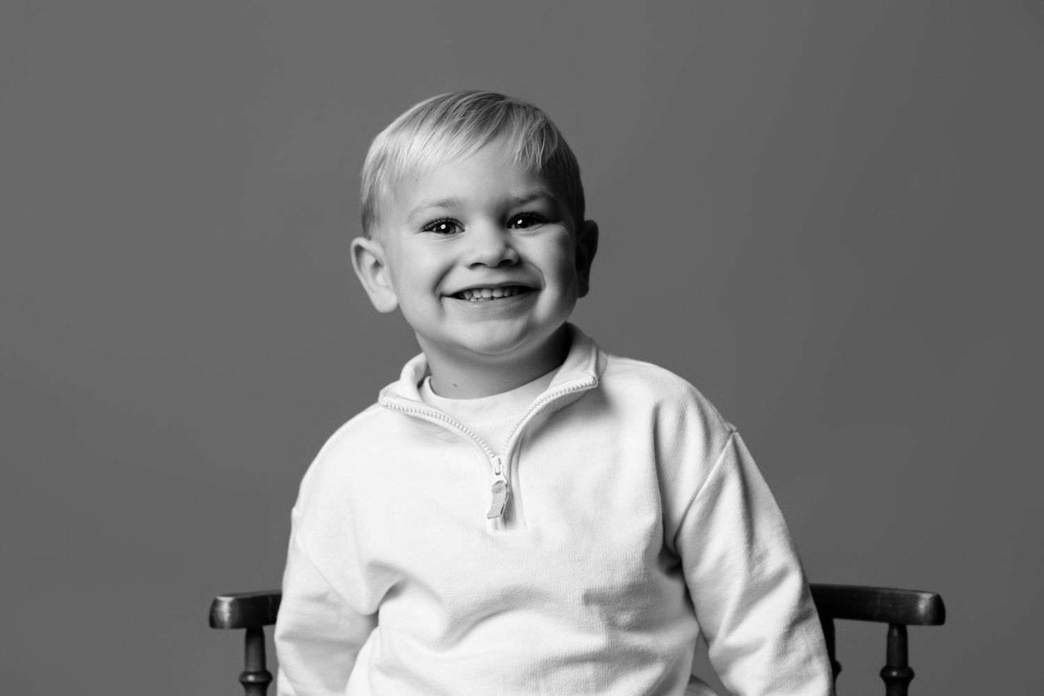 Sweet baby in white outfit smiling at camera against grey background.