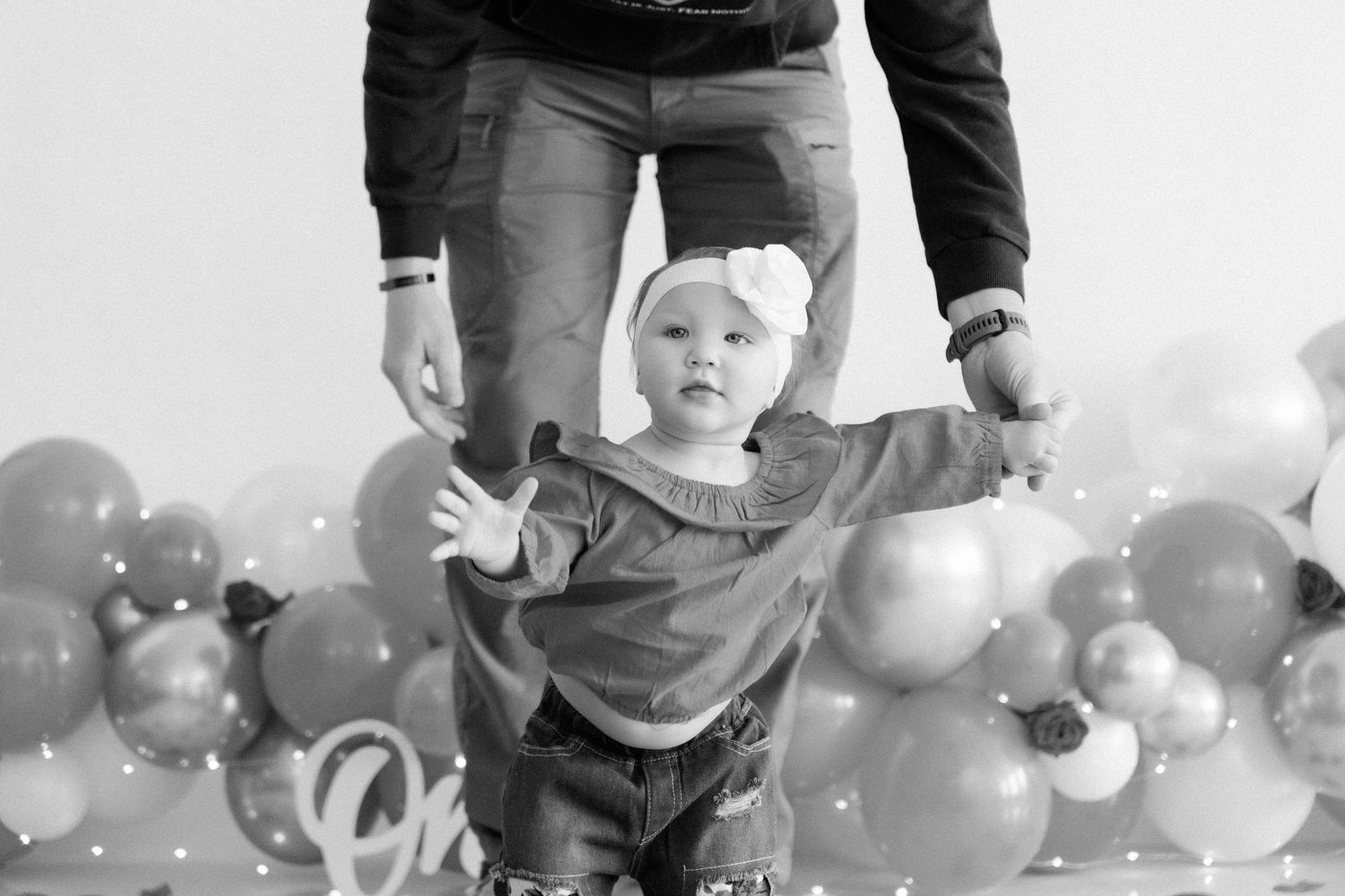 Young child sits in a chair surrounded by gray and white balloons at a celebration party.