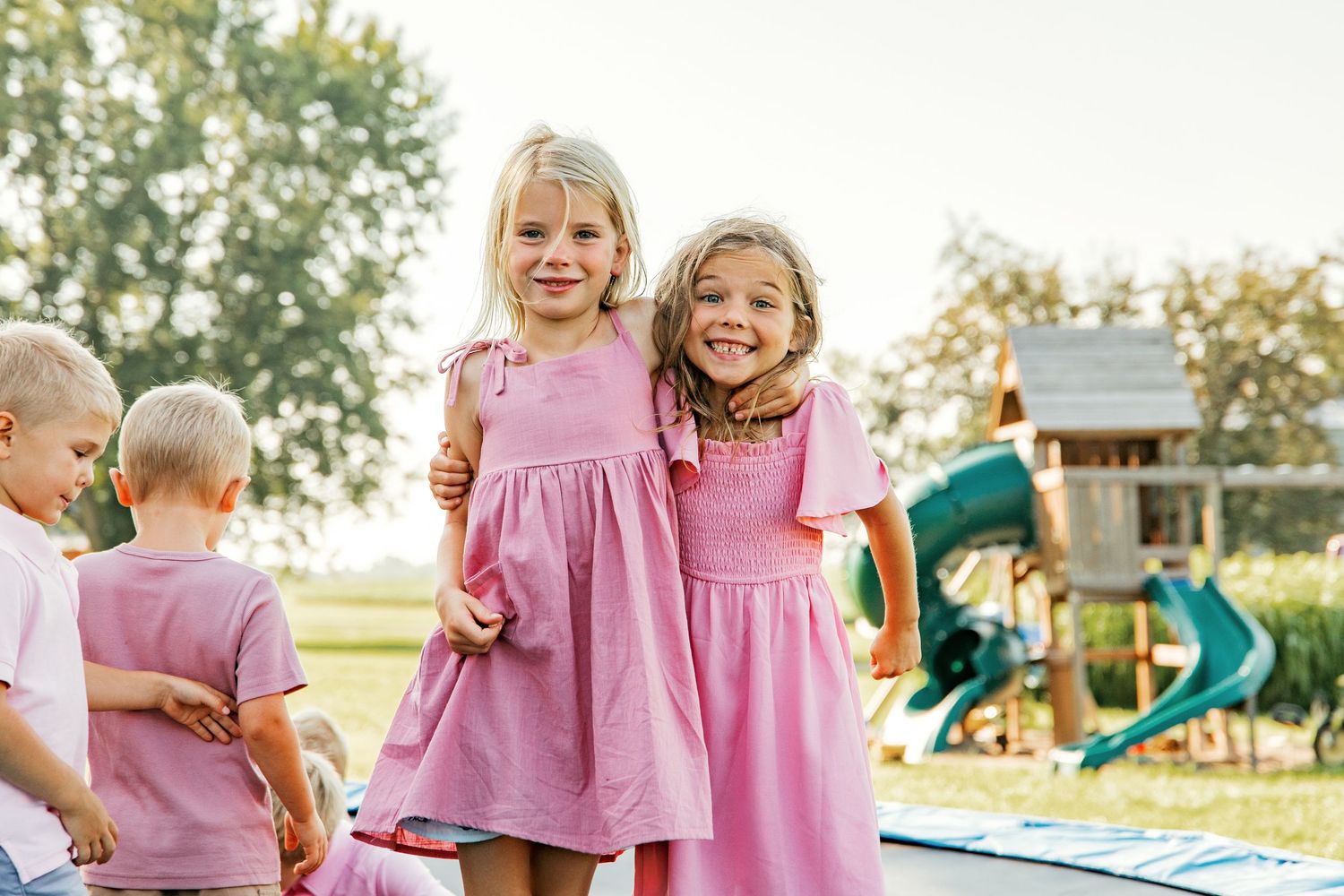 Children in pink and white outfits play together outdoors during a golden sunset at a playground.