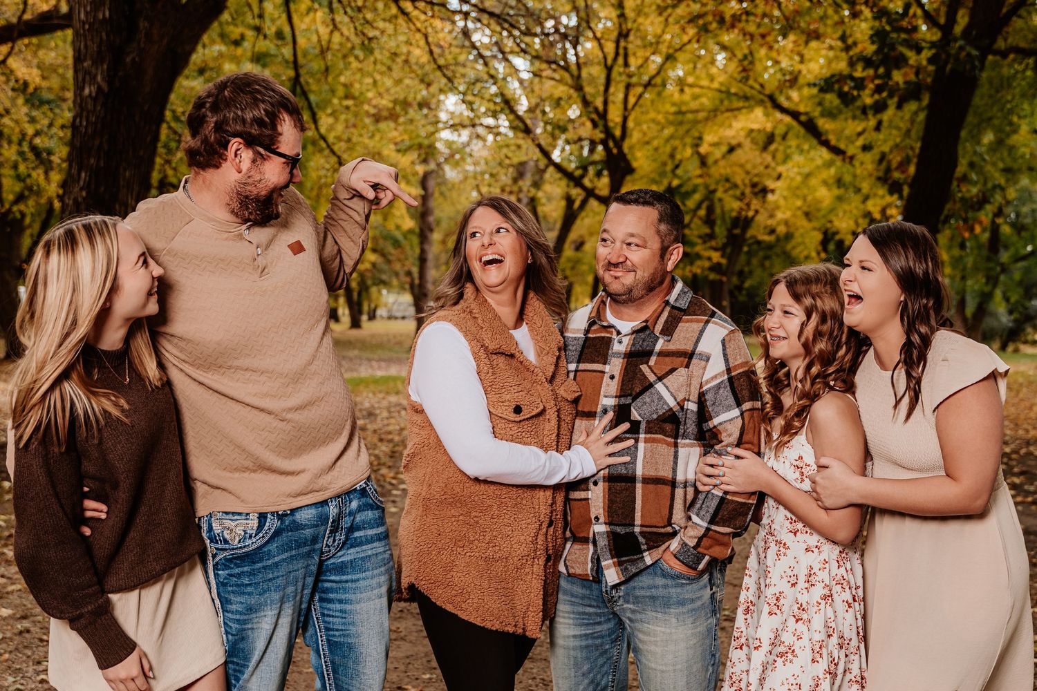 Family members share laughter while posing for photos outdoors during fall season.