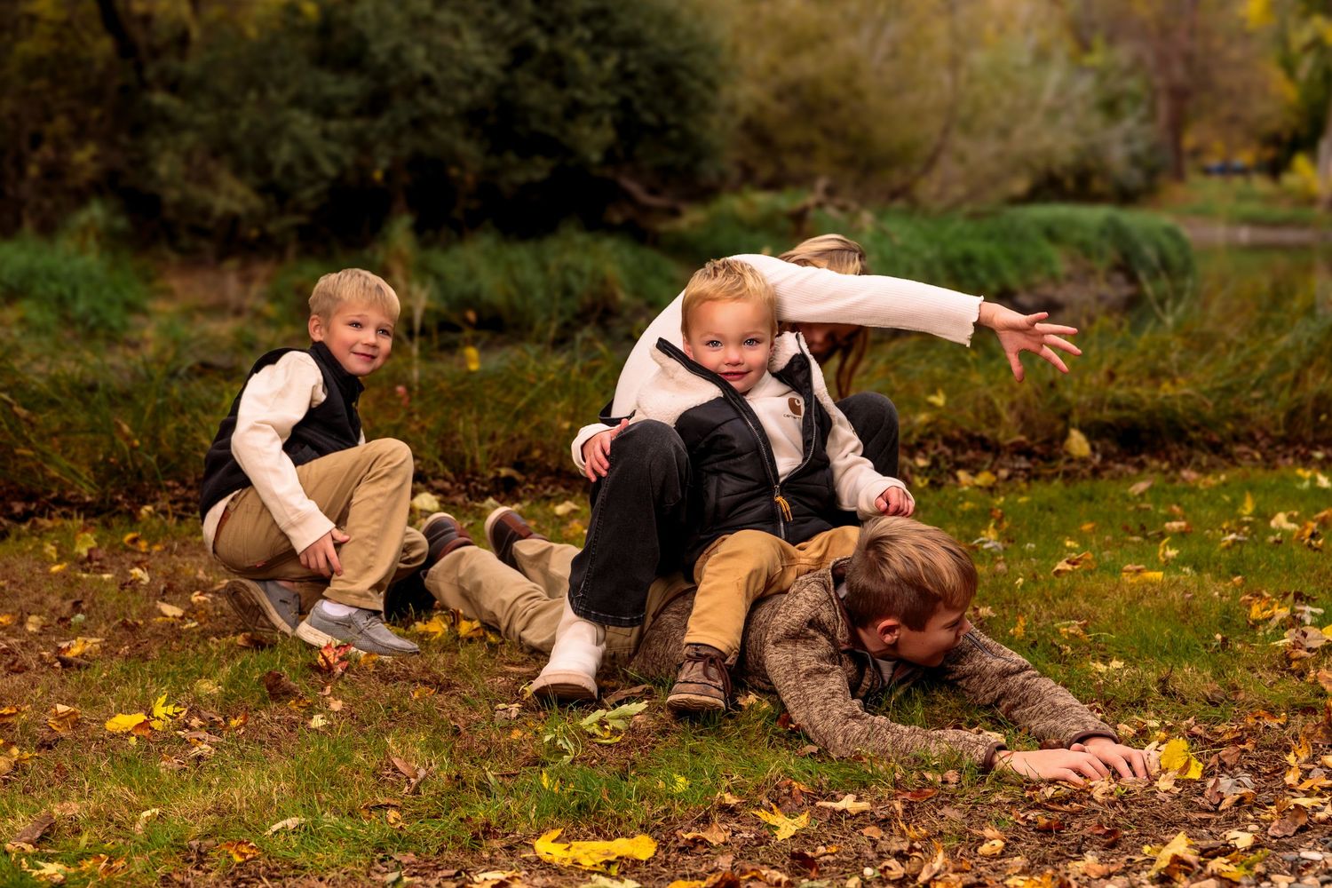 Family members lounging on autumn leaves in coordinated casual outfits during an outdoor photo session.
