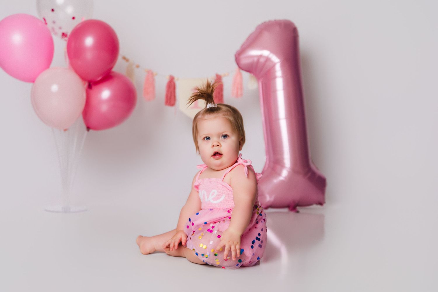 First birthday photo session with pink balloons and a baby in a floral pink outfit.