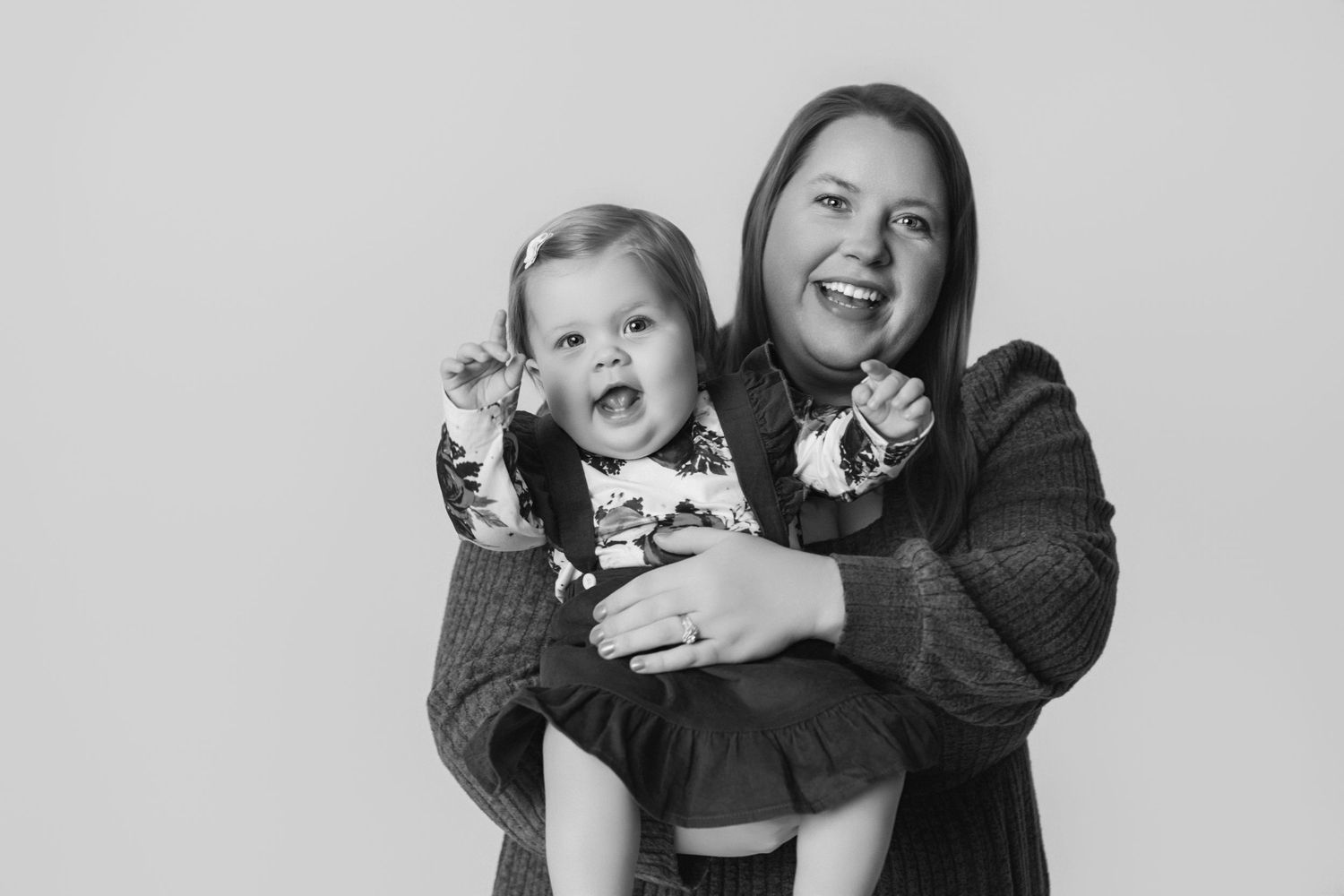 Black and white portrait of mother and baby laughing together in matching sweaters.