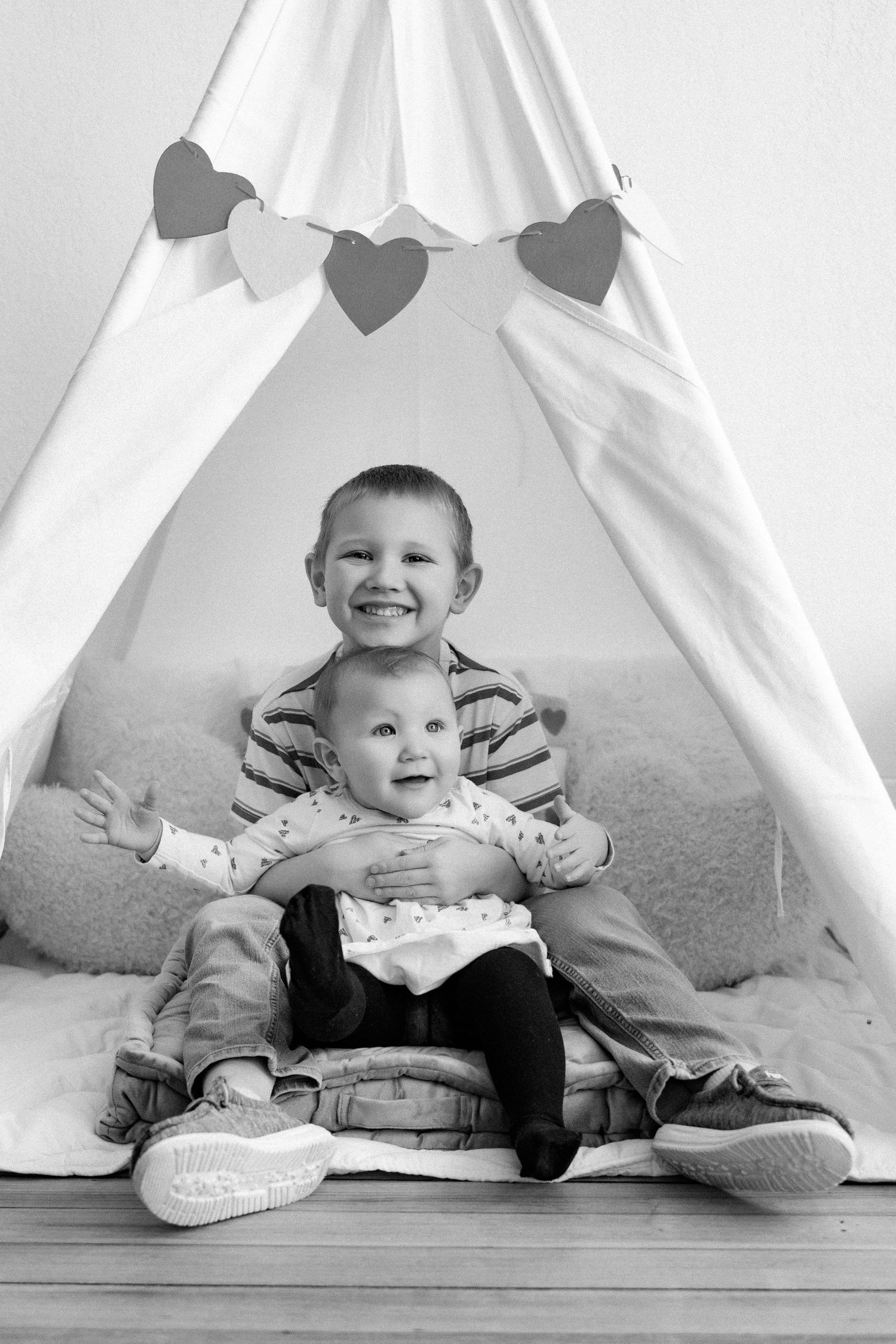 Black and white photo series showing a baby lying under a white teepee tent on a carpeted floor.