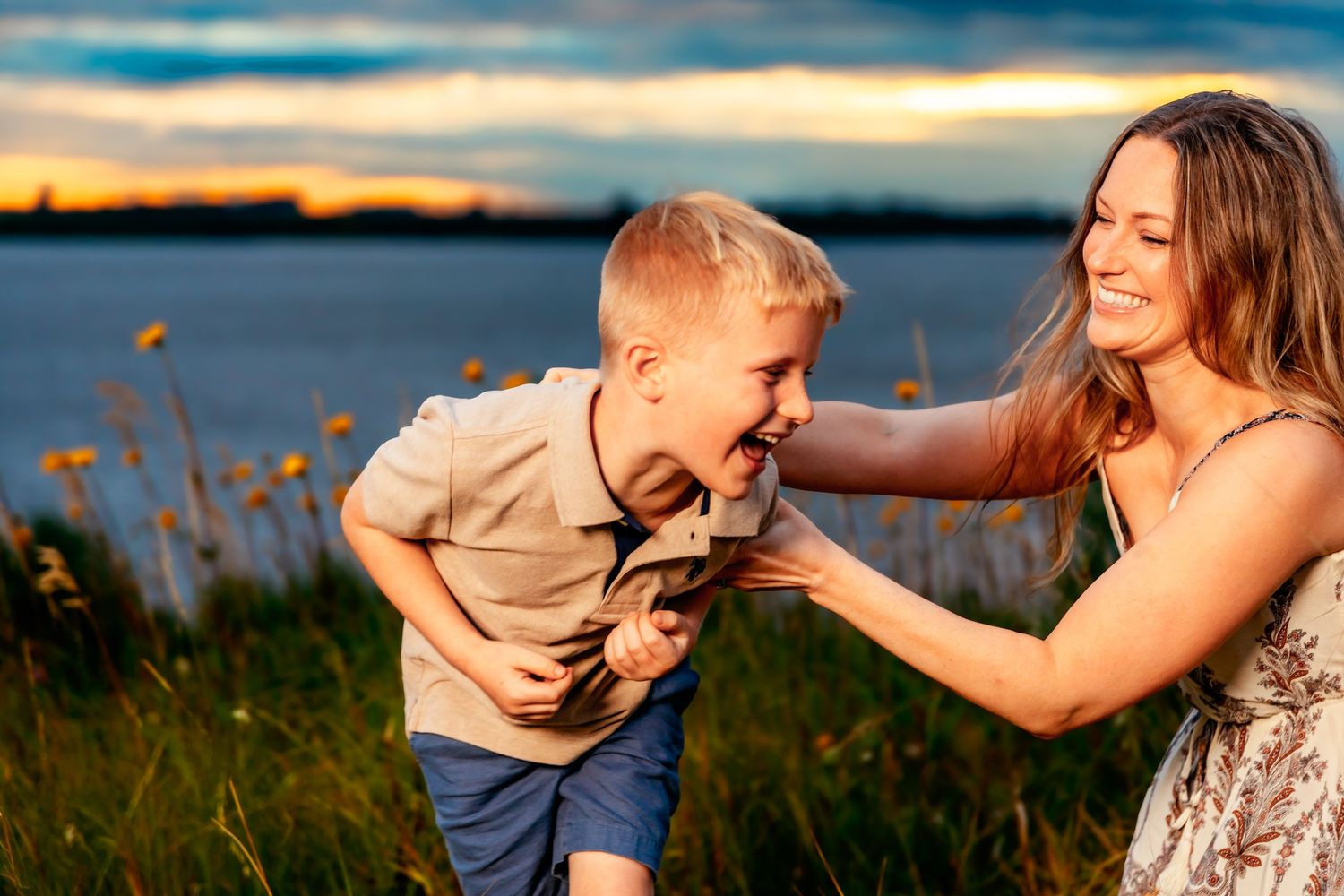 Two people share a joyful moment together in a field during sunset, with golden light illuminating their playful interaction.