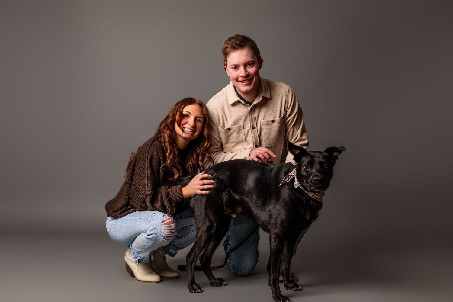 A series of candid studio portraits showing playful interactions between people and a black dog against a gray backdrop.