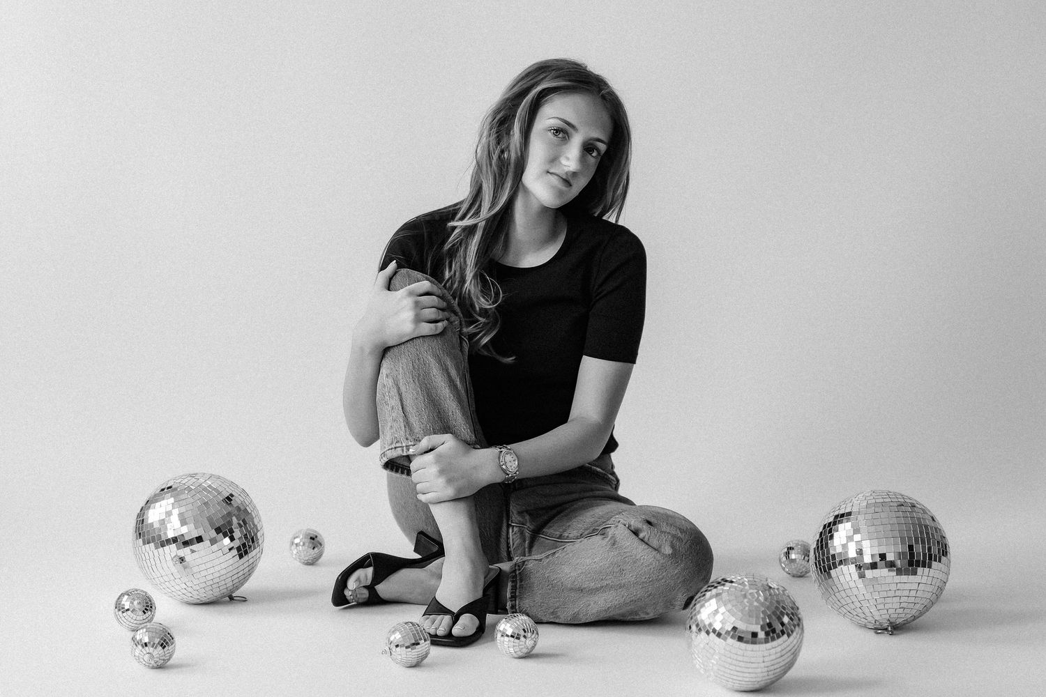 Woman in black tee and jeans posed with disco balls in black and white photo.
