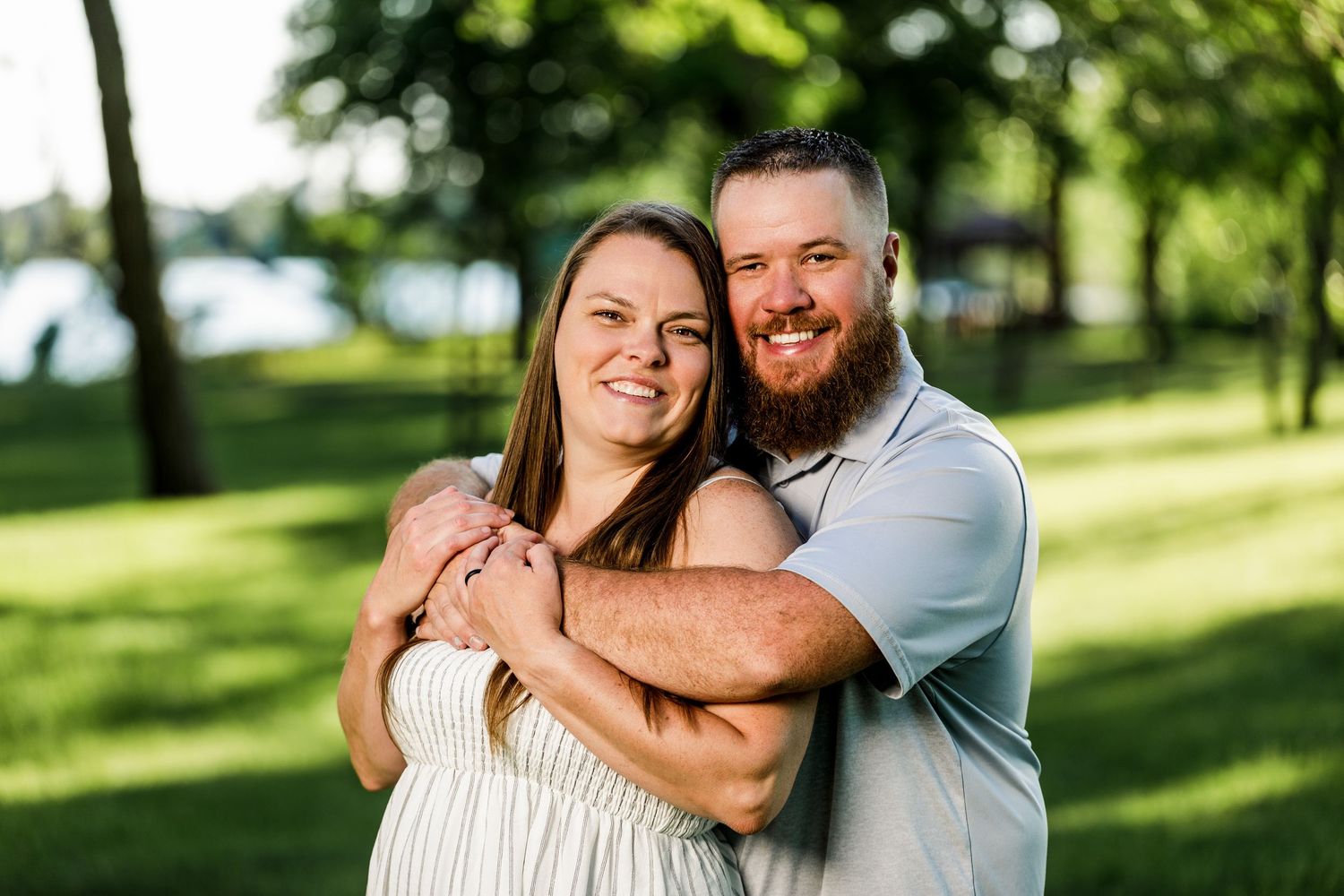Happy couple embracing and smiling outdoors near a lake on a sunny day.