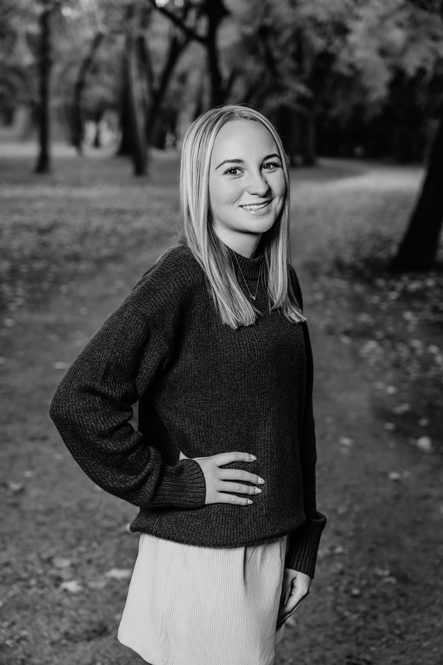 A woman in a black sweater poses outdoors during autumn with a playful expression.