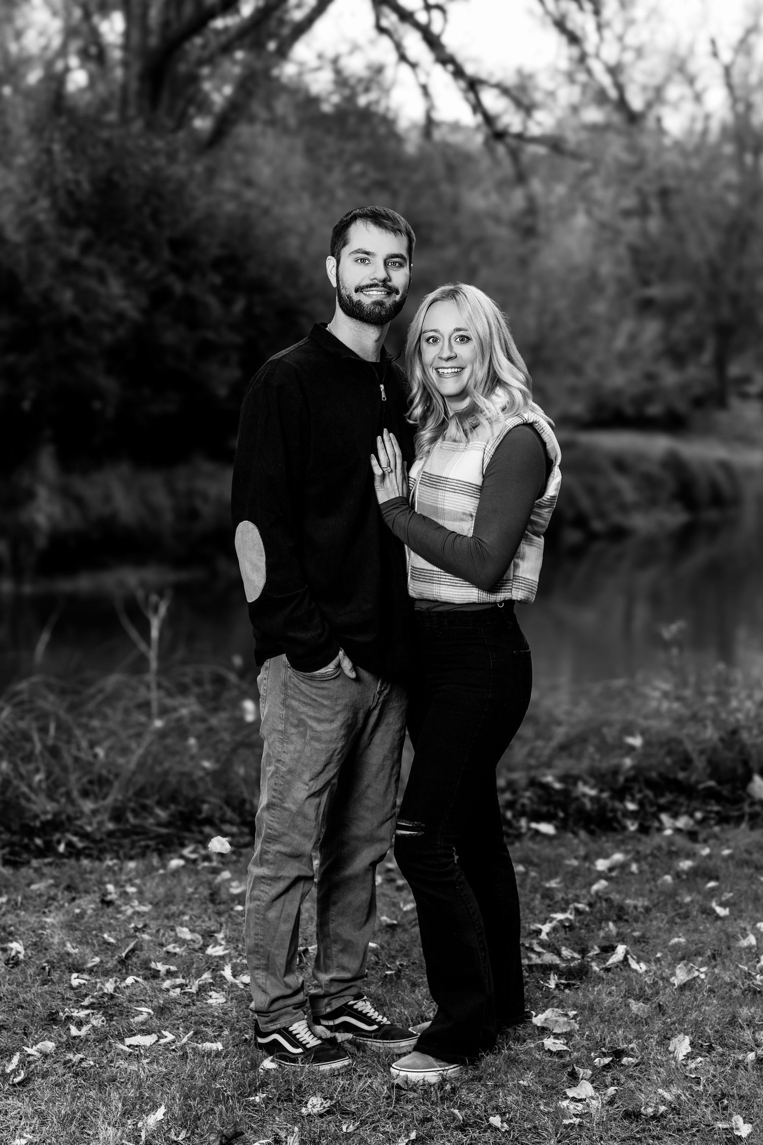 Black and white photo of couple sharing playful moment outdoors in autumn setting.