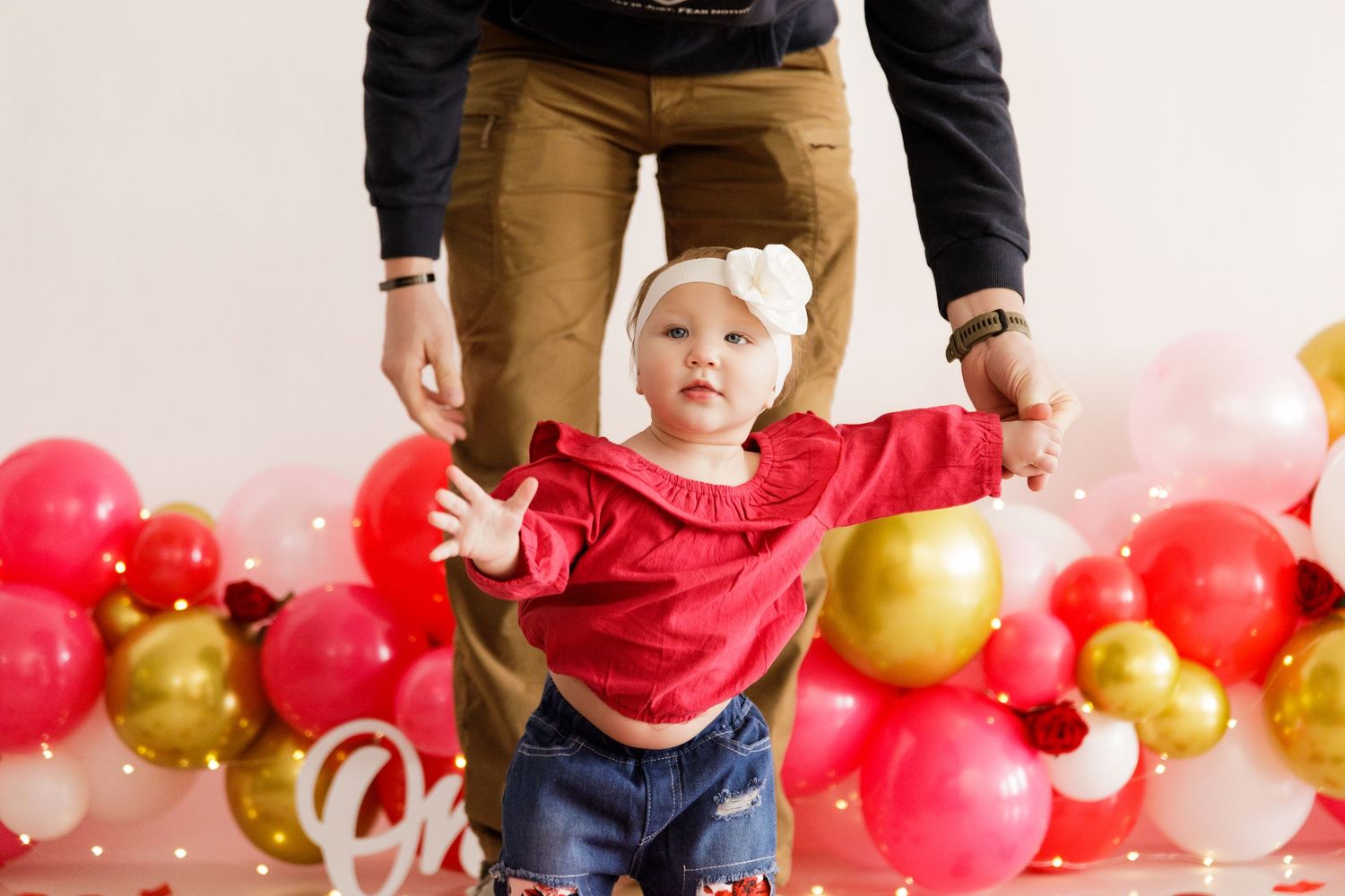Family photoshoot setup with red and gold balloon arch and white backdrop.