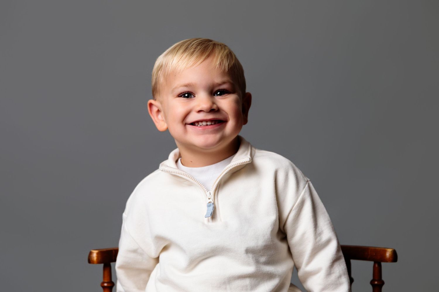 Young child in white collared shirt sitting against gray background with bright smile.