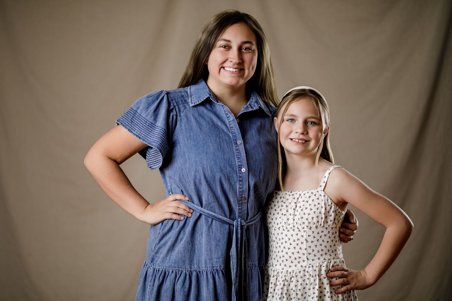 Woman in blue dress and young girl in floral dress posing together for a studio portrait photo.