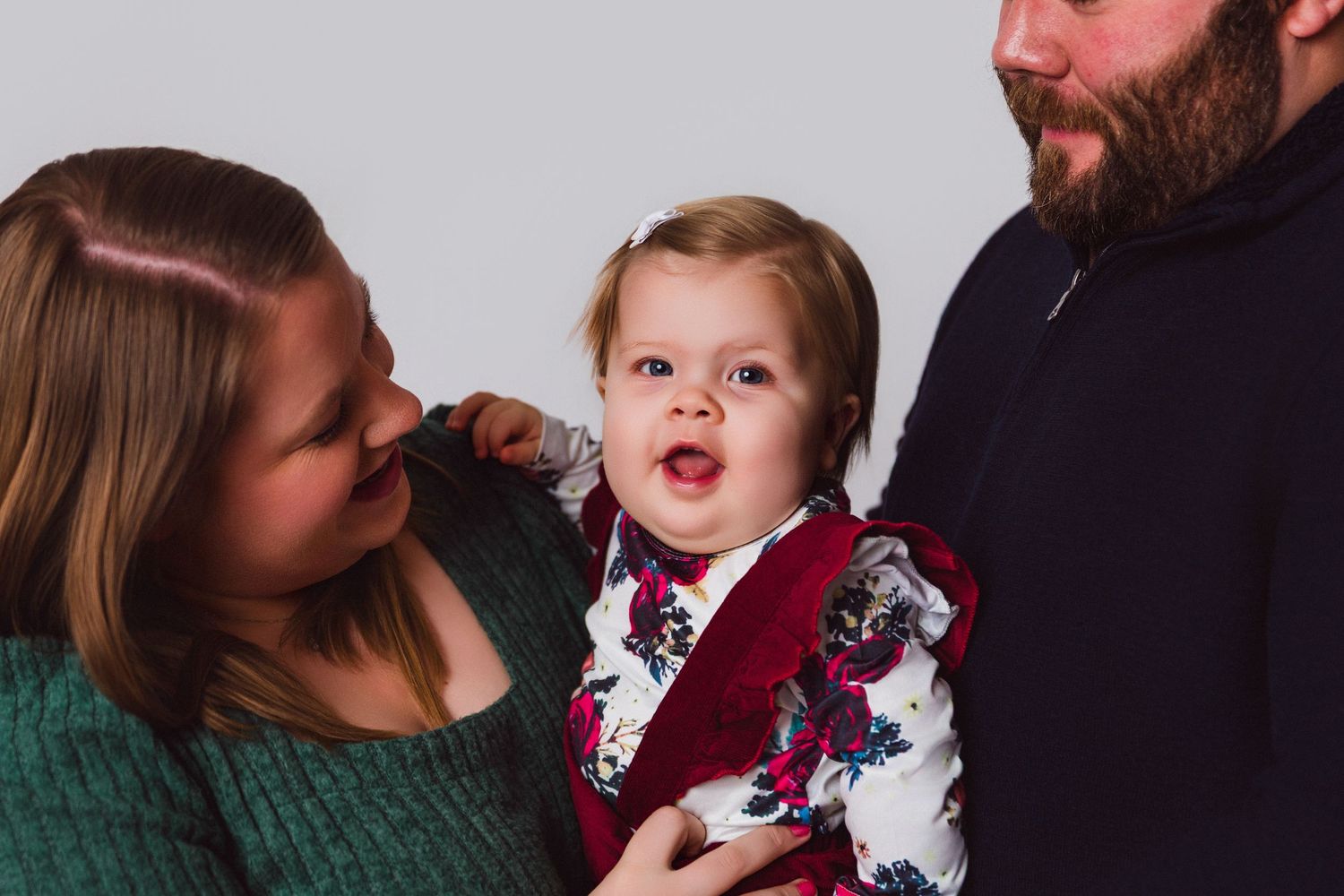 A tender family portrait in green and burgundy tones showing a playful moment together.