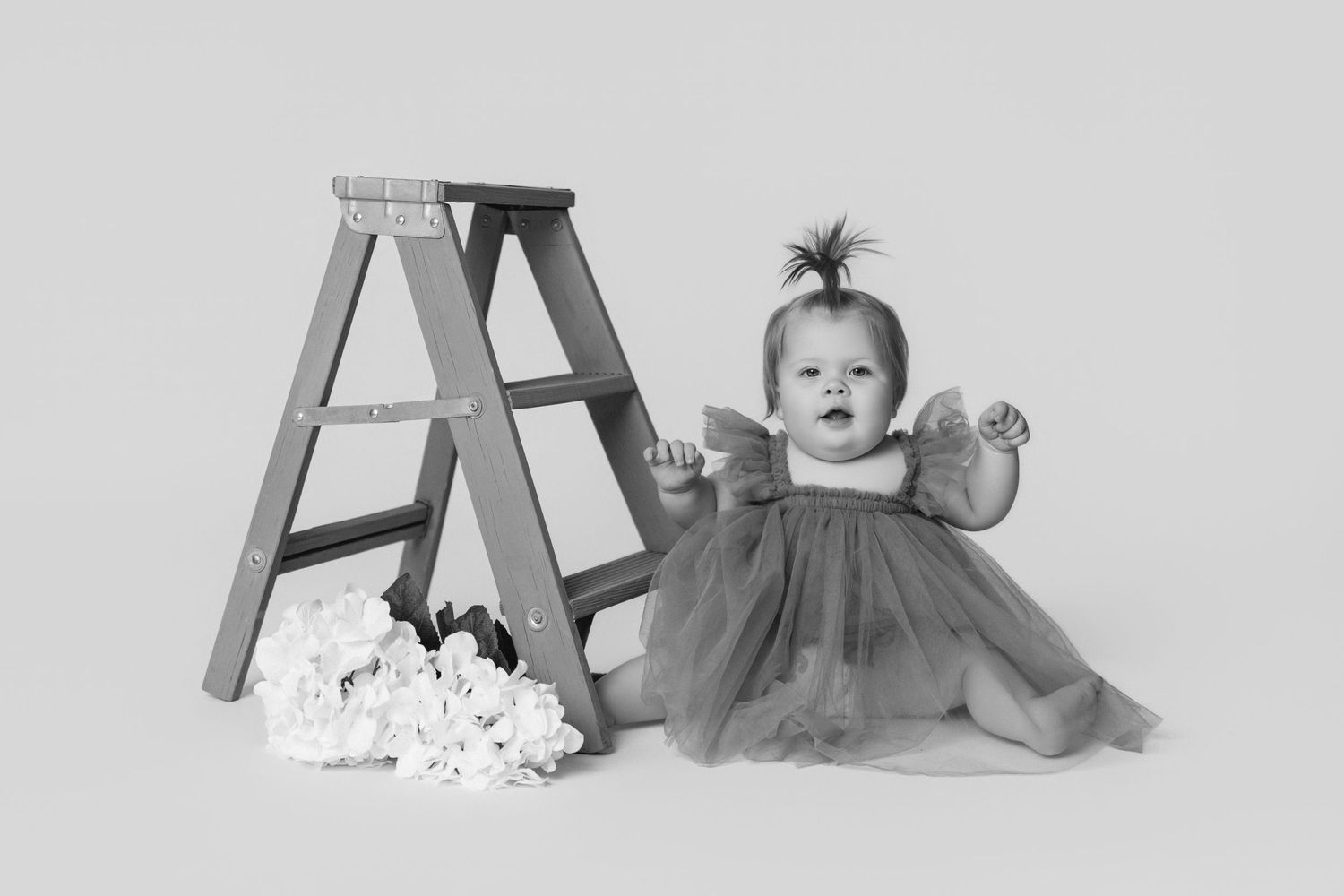 Studio portraits of a baby lying and playing near a green ladder with popcorn scattered around.