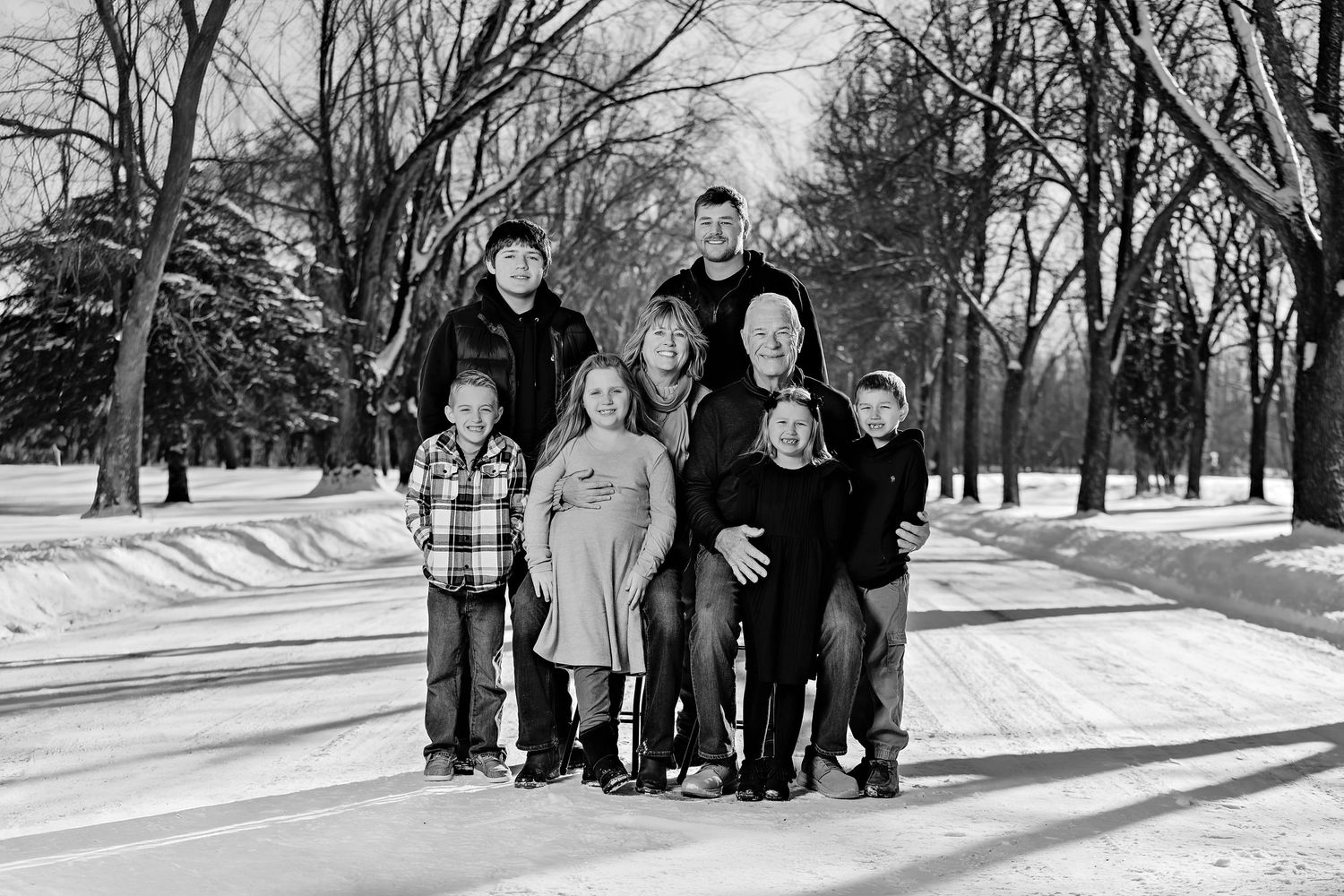 A small family group stands together in black and white on a snow-covered path with trees.