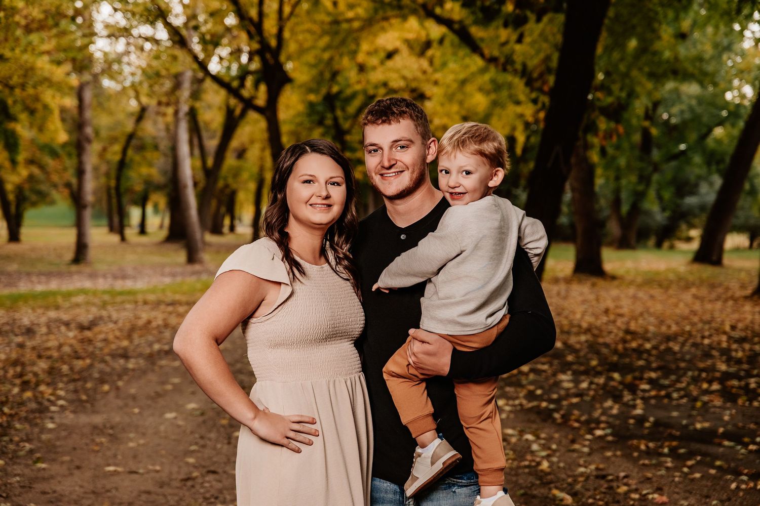 Family group poses together on leaf-covered path during autumn photo session.