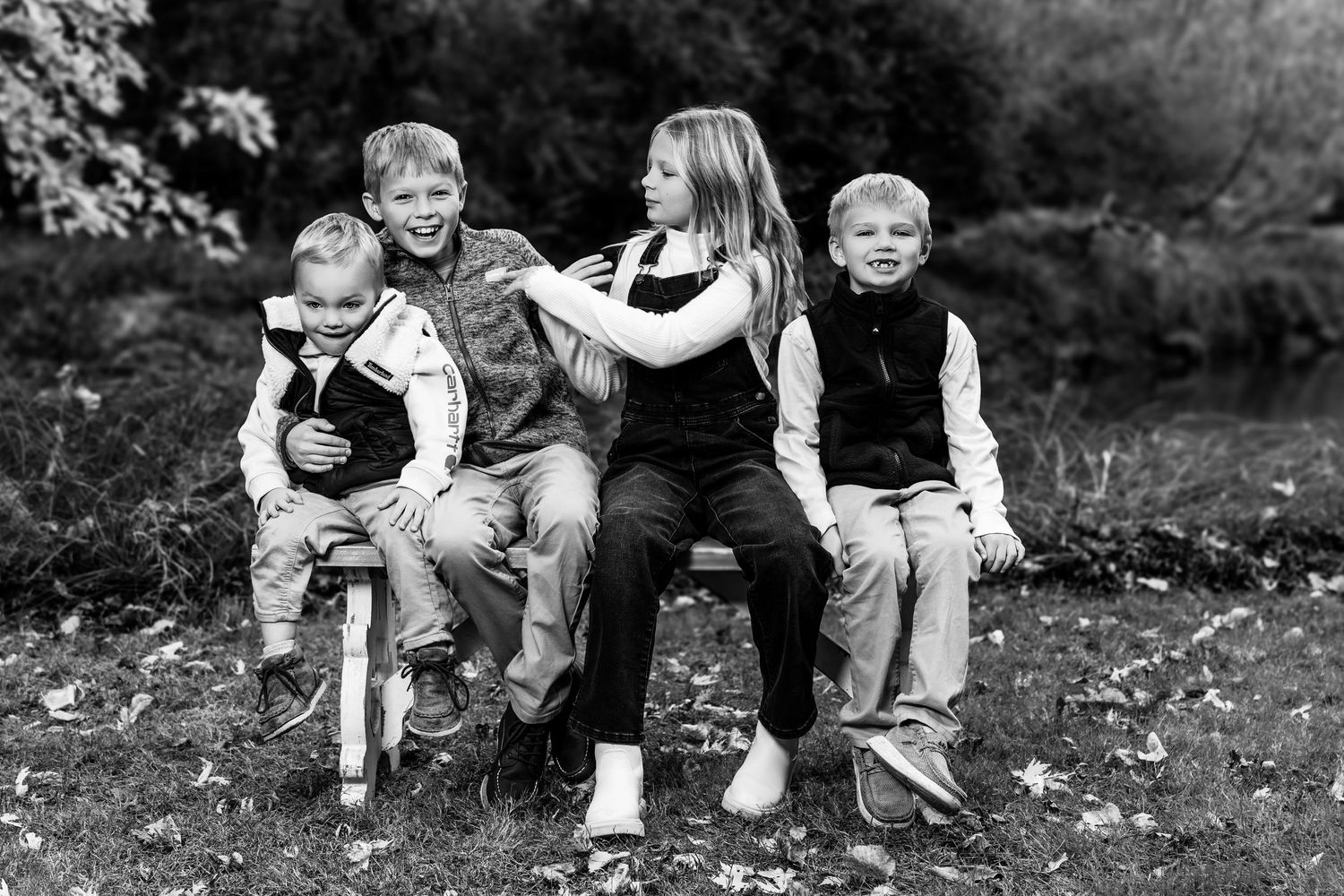 A monochrome outdoor family photo showing people seated together on fallen leaves.
