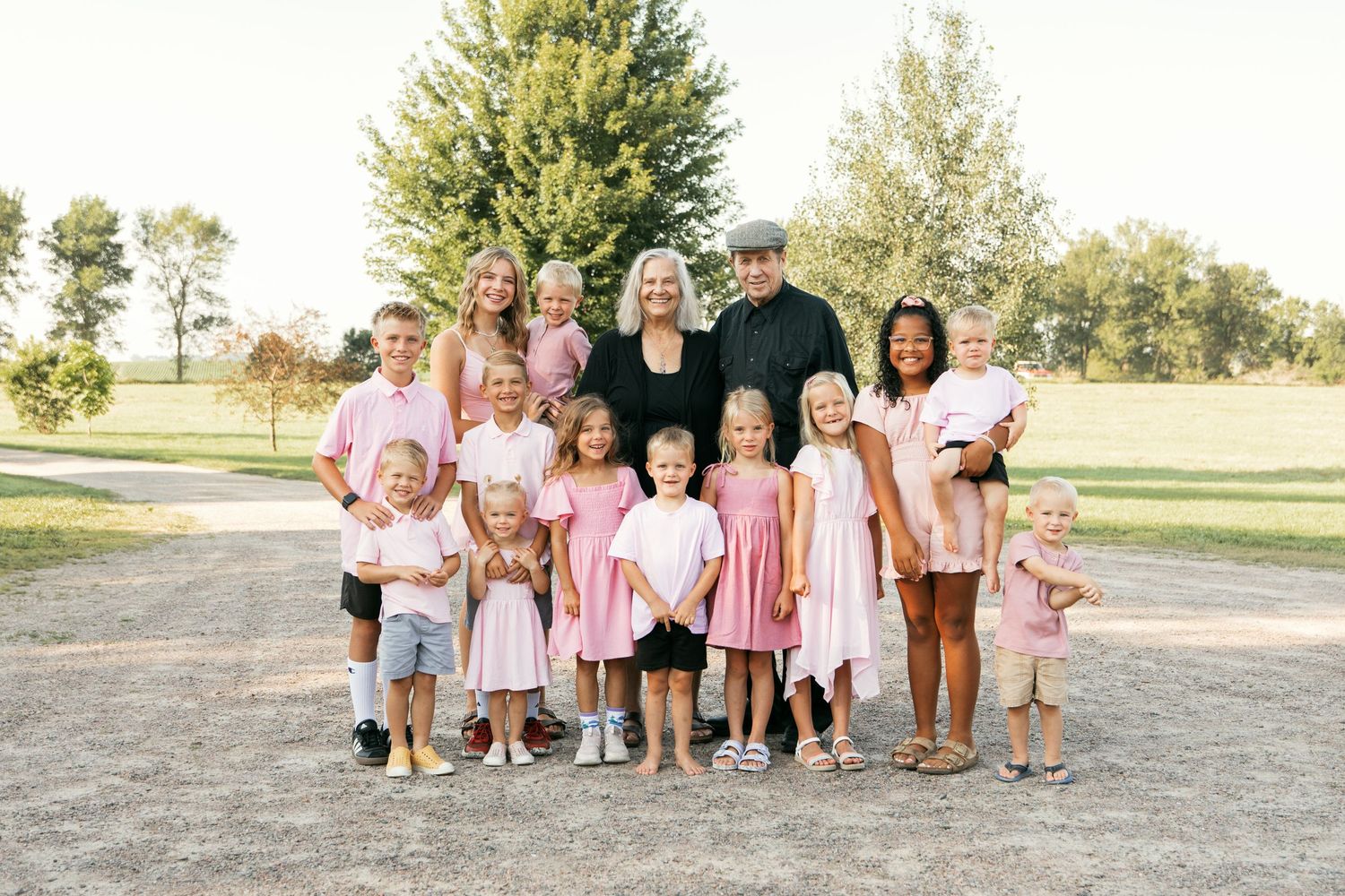 Large family group photo taken outdoors in a park setting with children and adults wearing pink and casual attire.