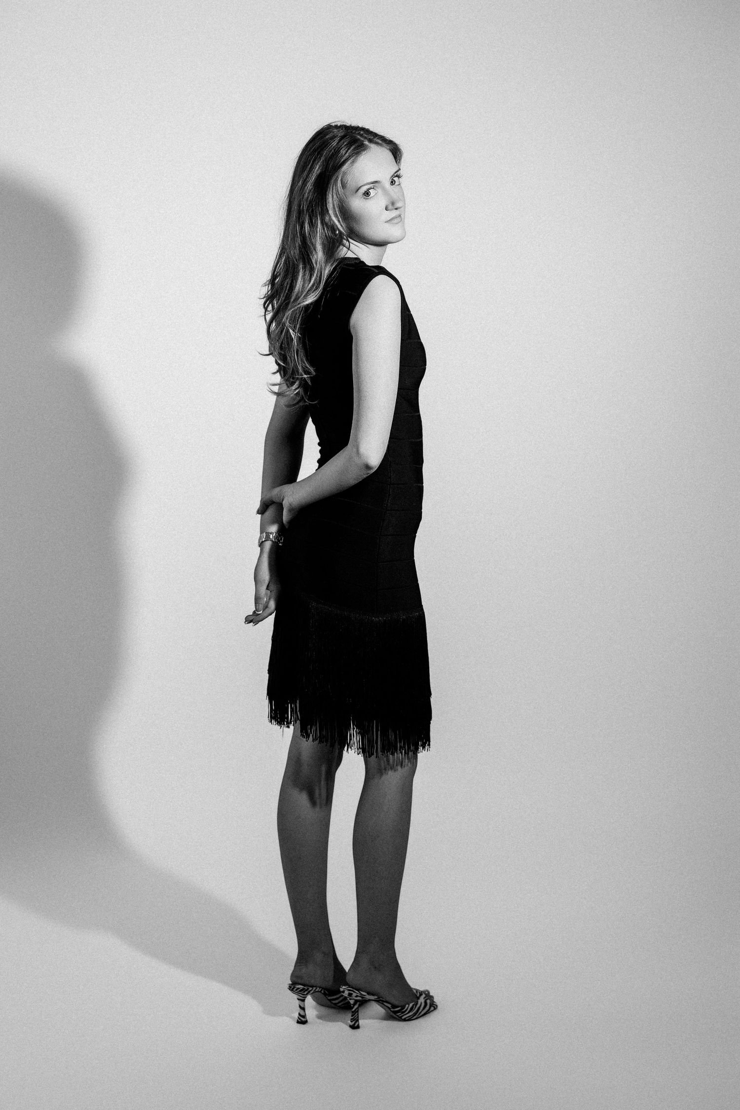 Young woman in black fringed dress viewed from behind in elegant black and white studio portrait.