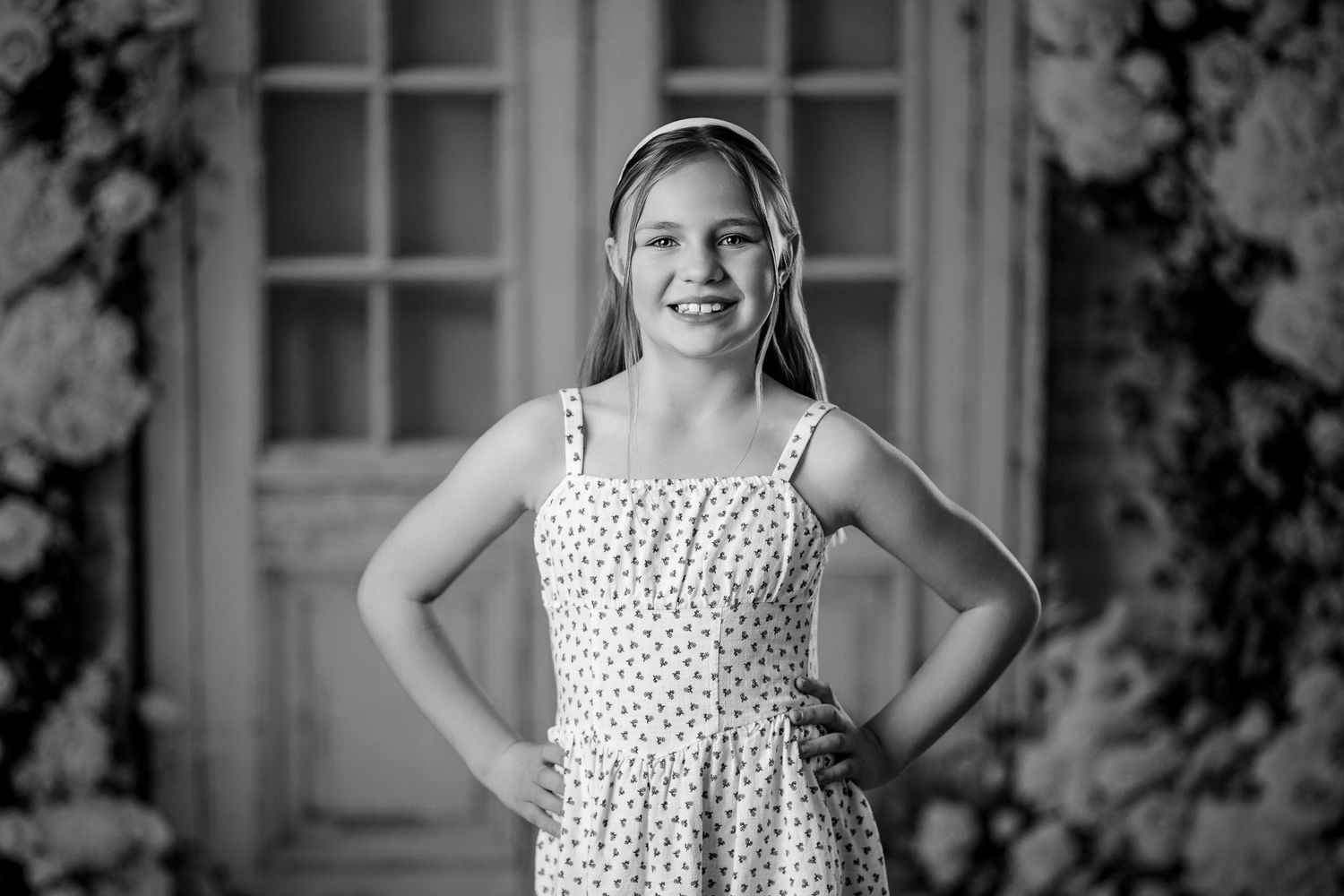 Black and white portrait of a smiling girl in a polka dot dress standing with hands on hips.