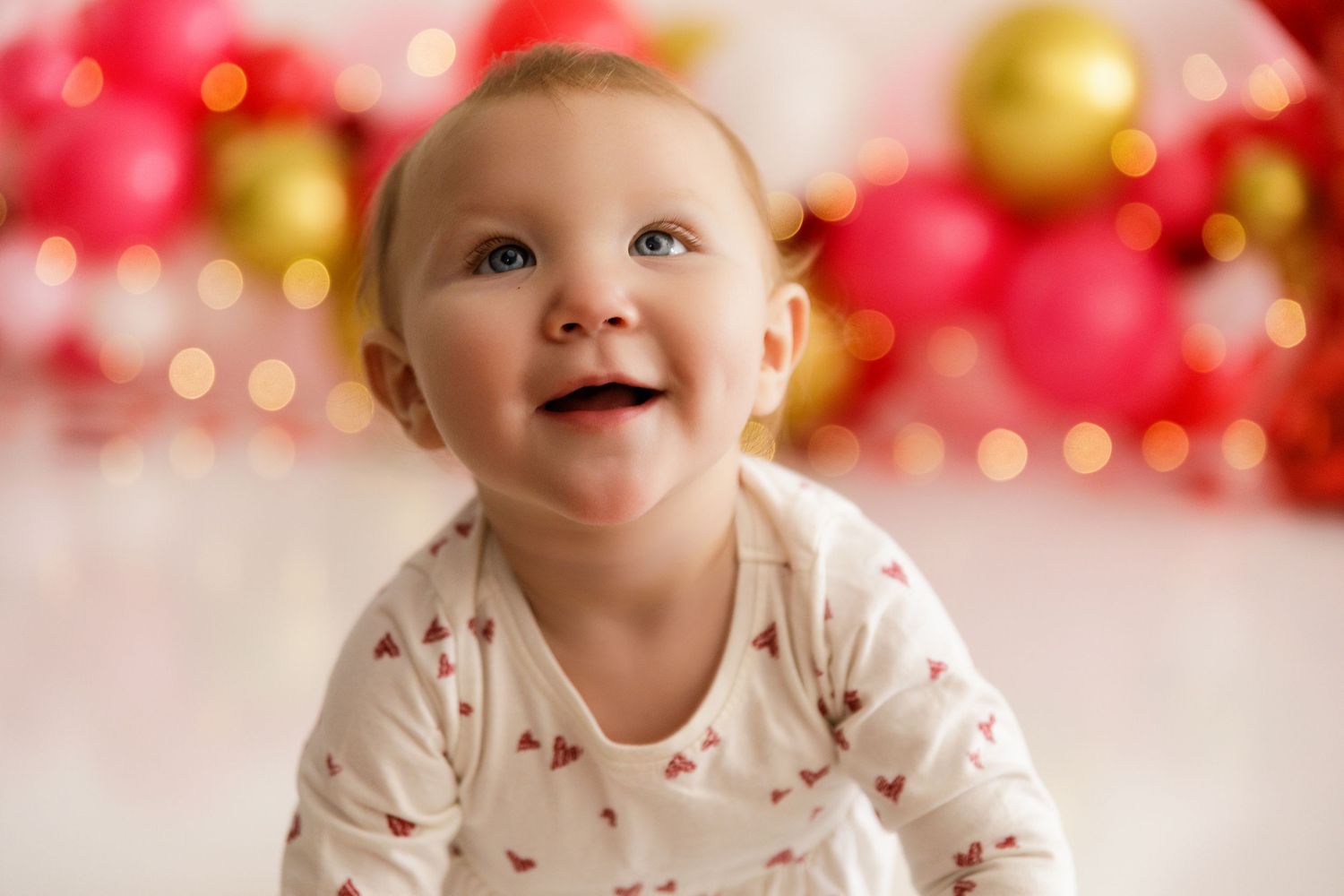 Baby photoshoot setup with pink and gold balloon garland and white background.