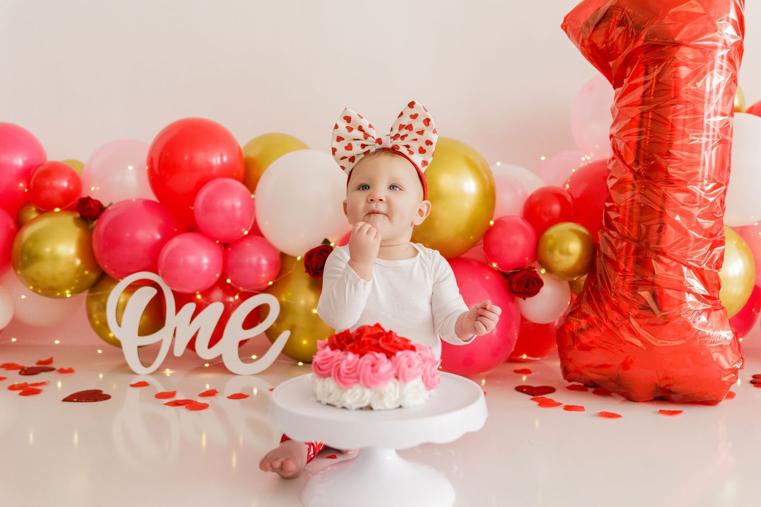 First birthday party decorations featuring red and gold balloons with number one balloon and 'ONE' sign.