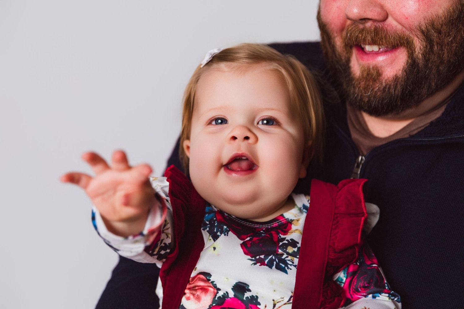 Multiple shots of a baby in a red dress making expressive faces while being held.