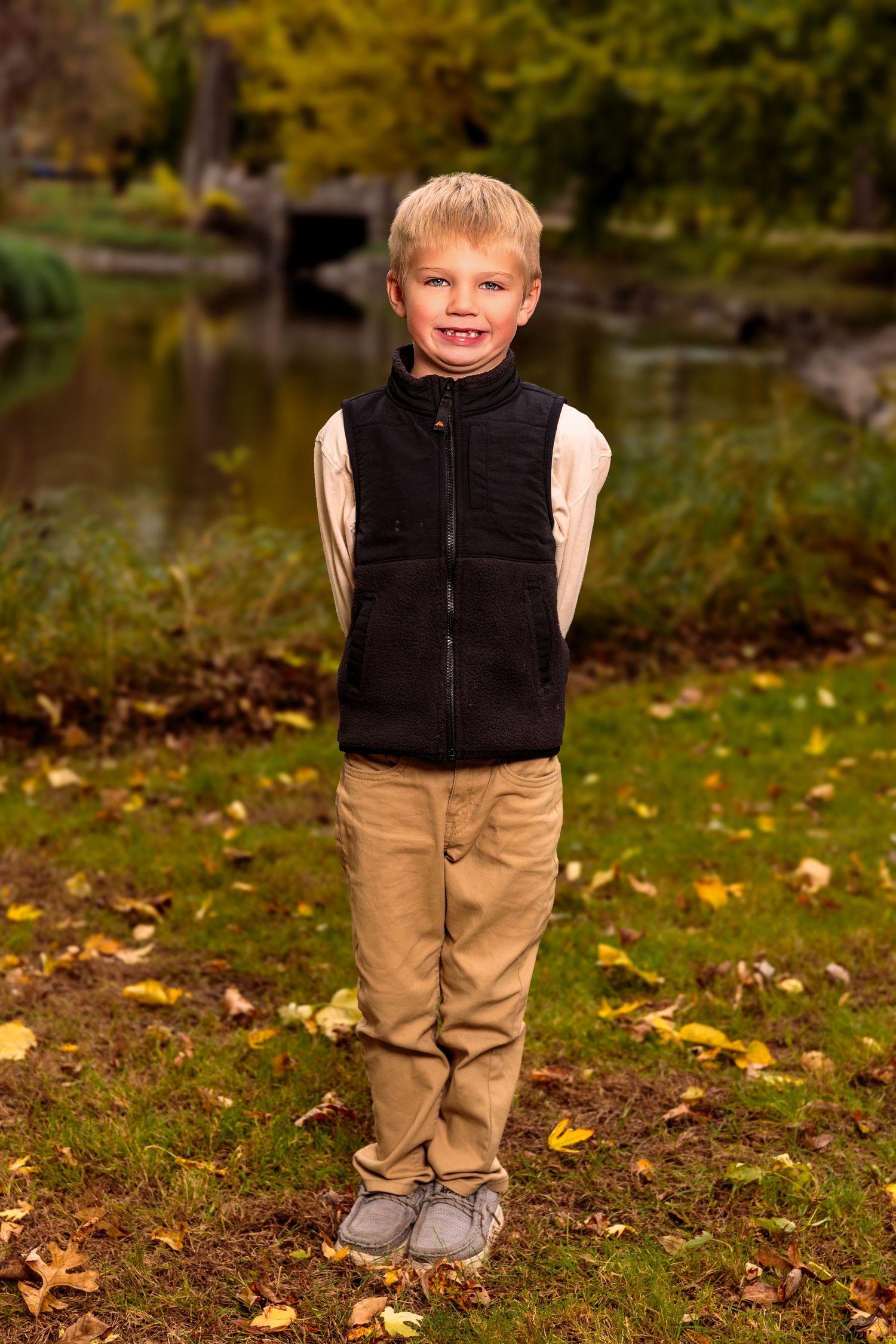 Child in black vest and khaki pants standing on fallen leaves during autumn.