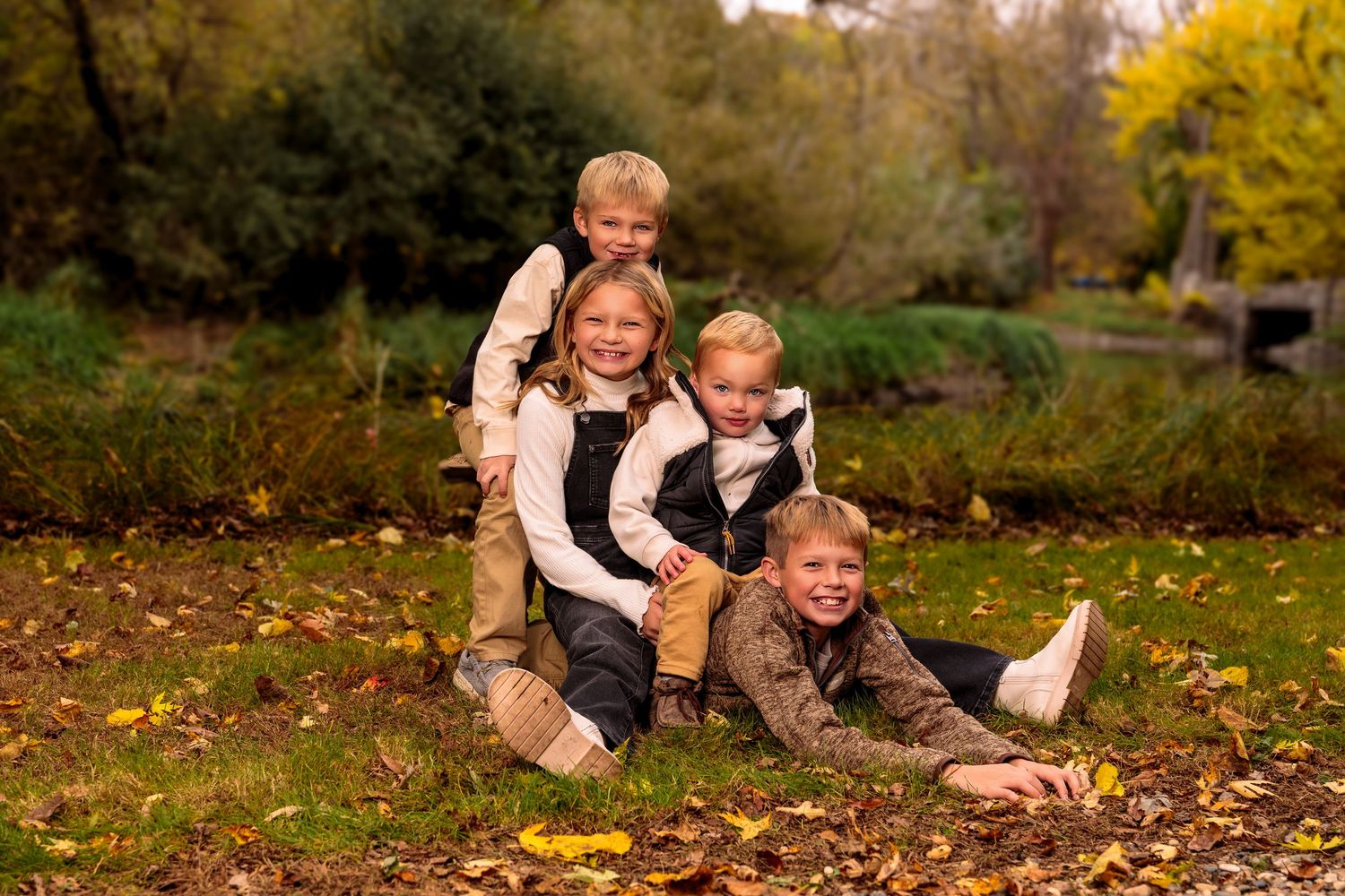A playful family moment captured outdoors among fallen autumn leaves near a pond.