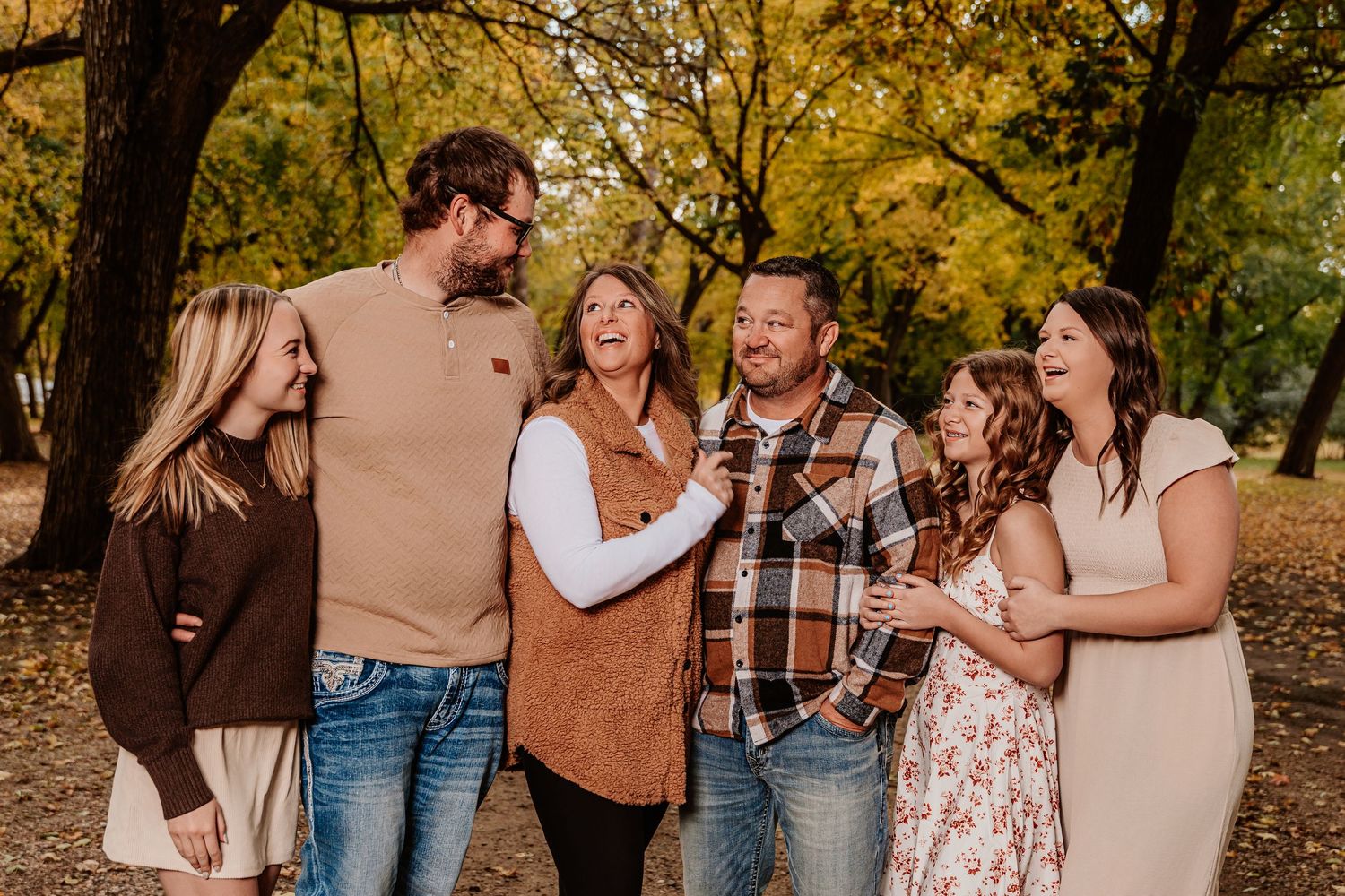 A group enjoys a candid moment together during an autumn photoshoot in a park with golden leaves.