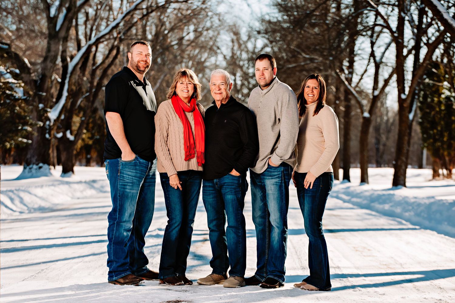 A small family group poses together on a snowy path with bare winter trees in the background.