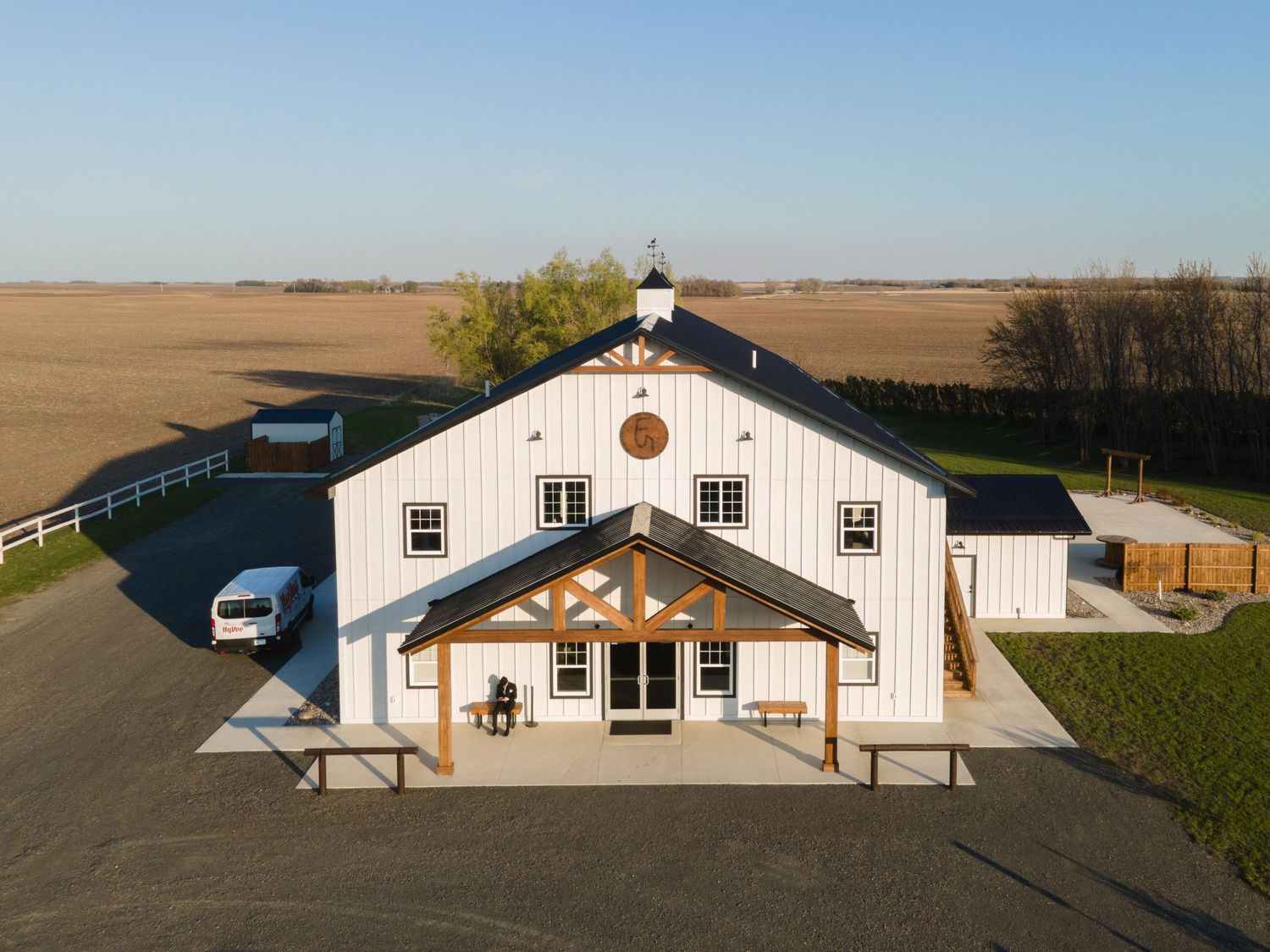 A panoramic view of a white barn with black trim set against rolling farmland and clear blue sky.